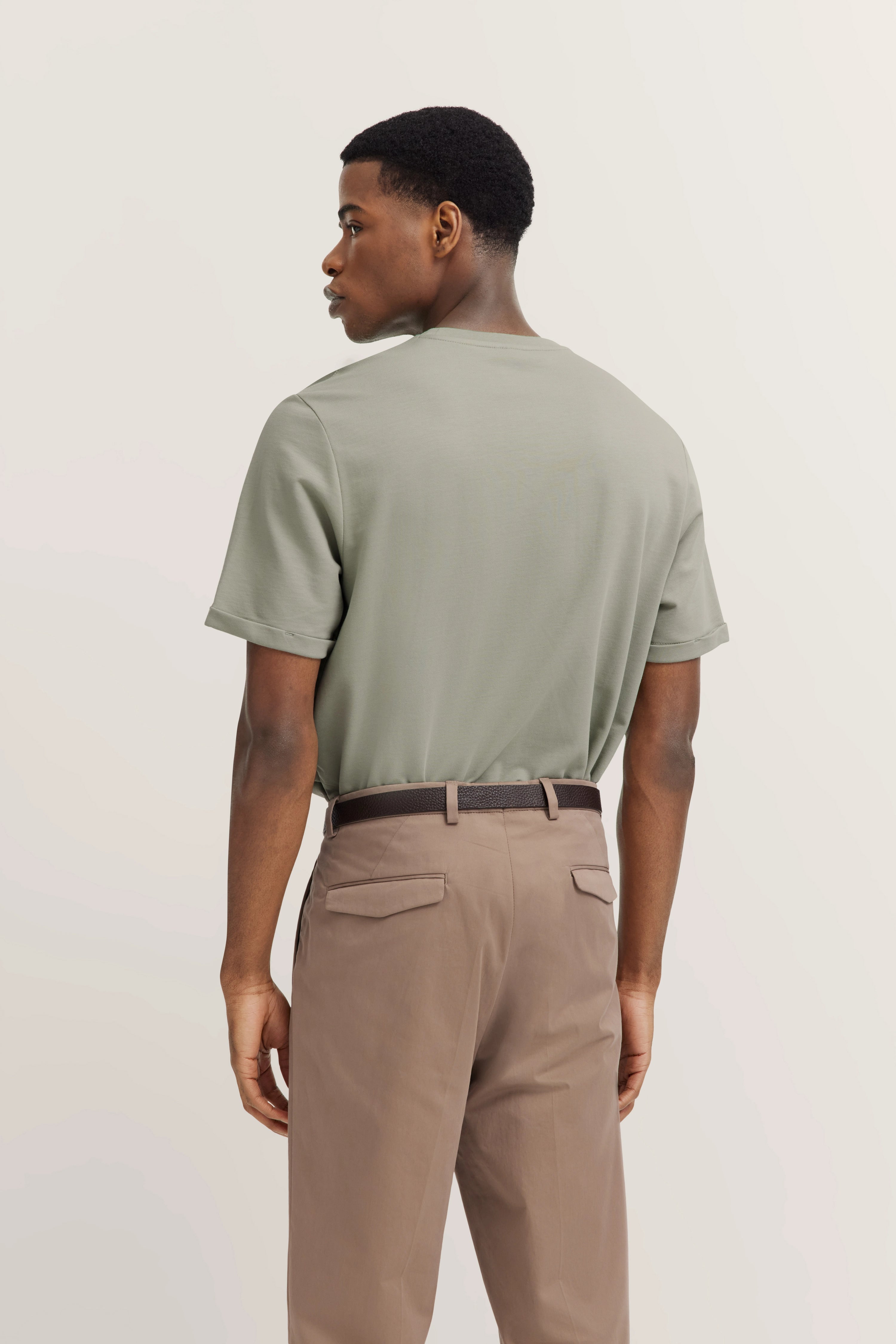 Model in olive T-shirt and brown pants by bugatti, standing sideways.