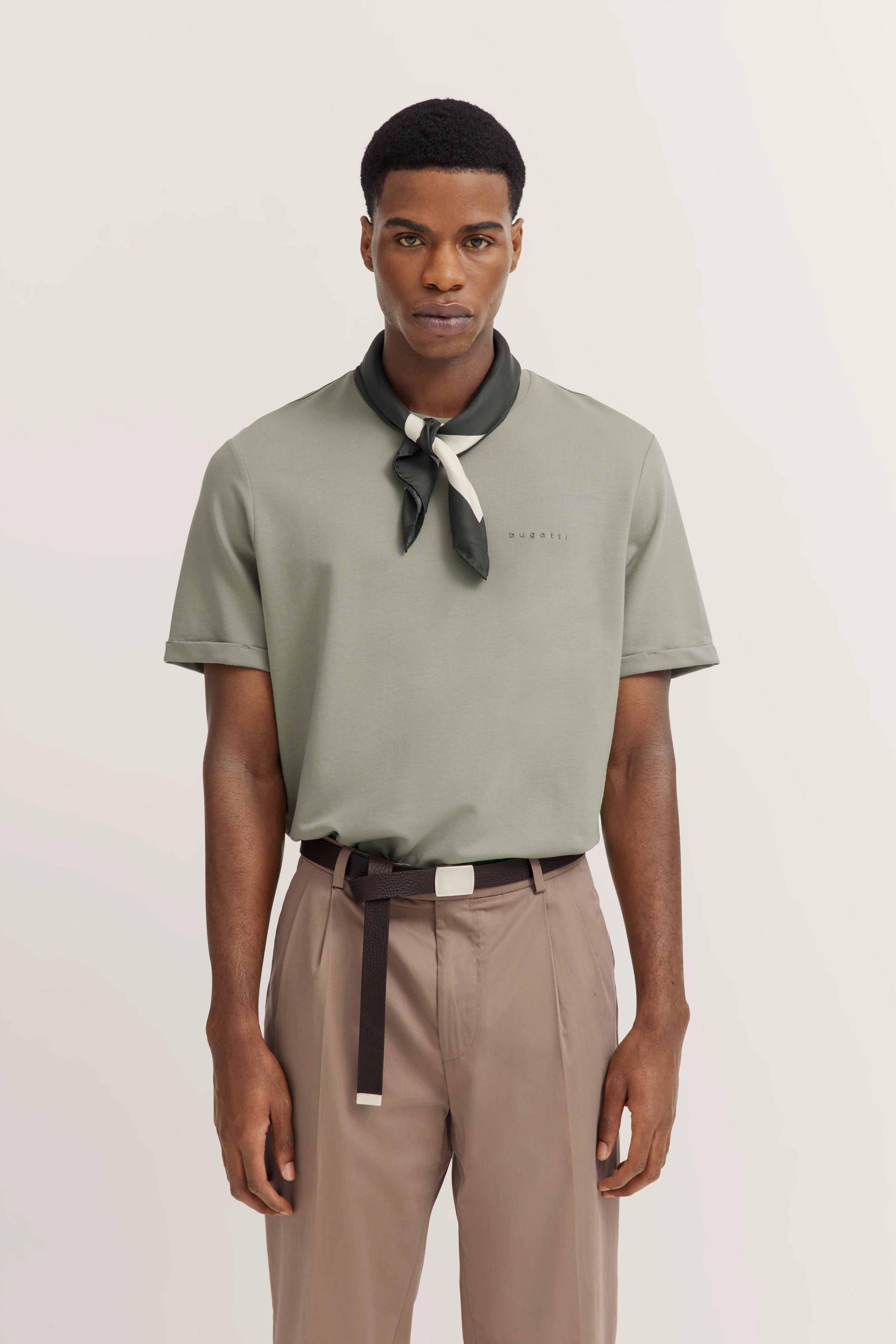 Model in gray bugatti shirt, beige pants, black scarf, relaxed pose.