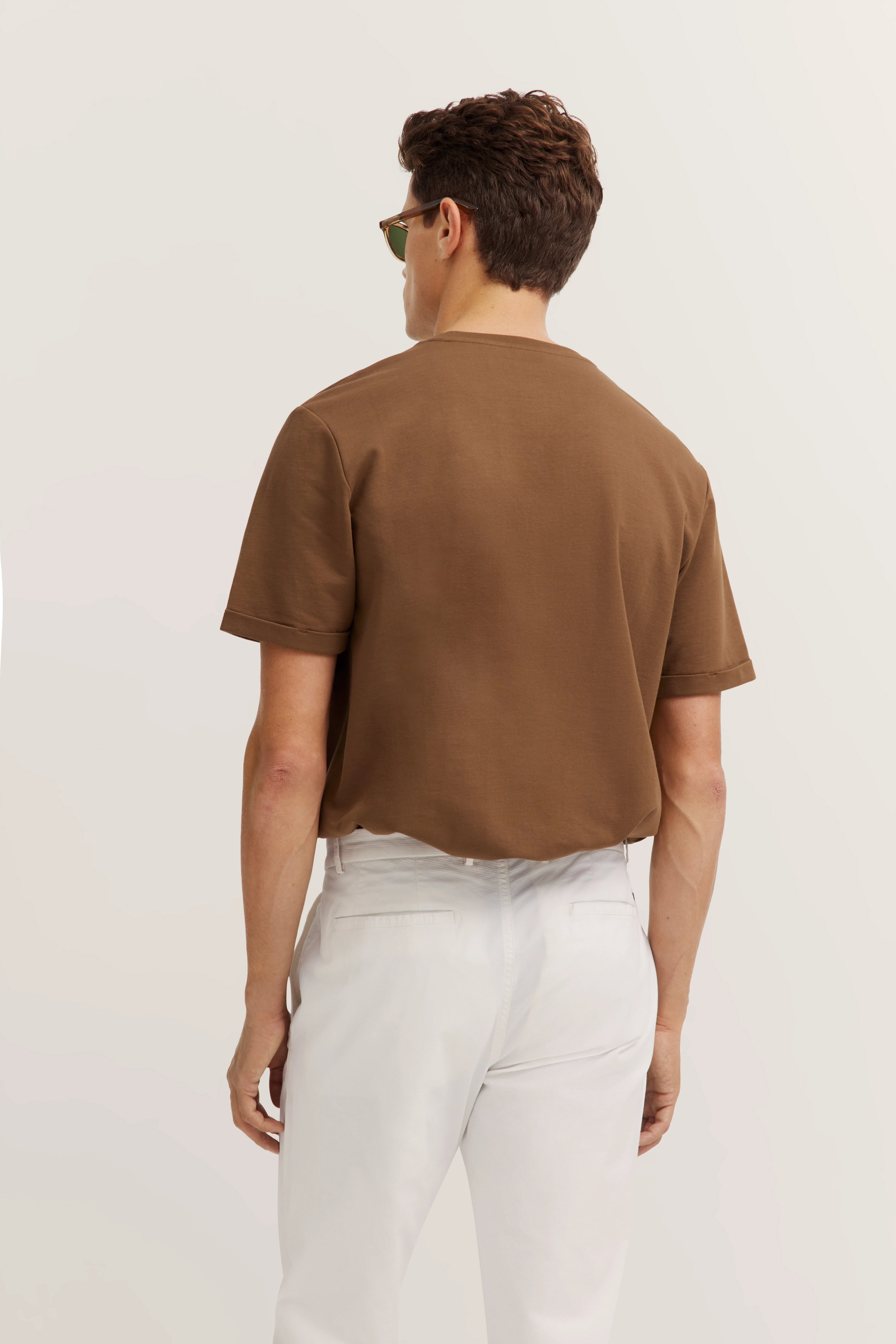 Brown T-shirt and white pants, rear view, casual model image, relaxed pose.