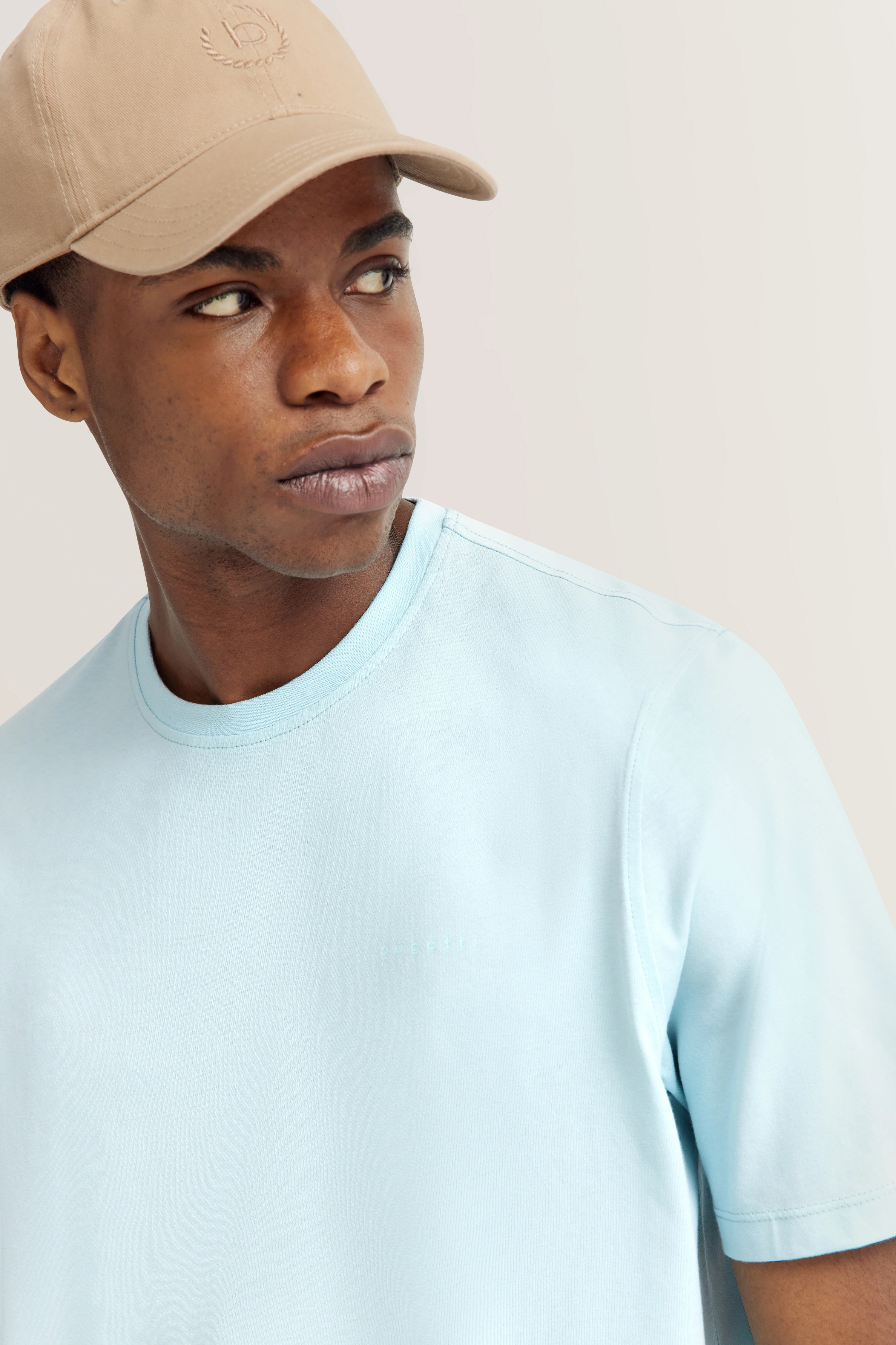 Model in light blue bugatti T-shirt and beige cap, three-quarter profile view.