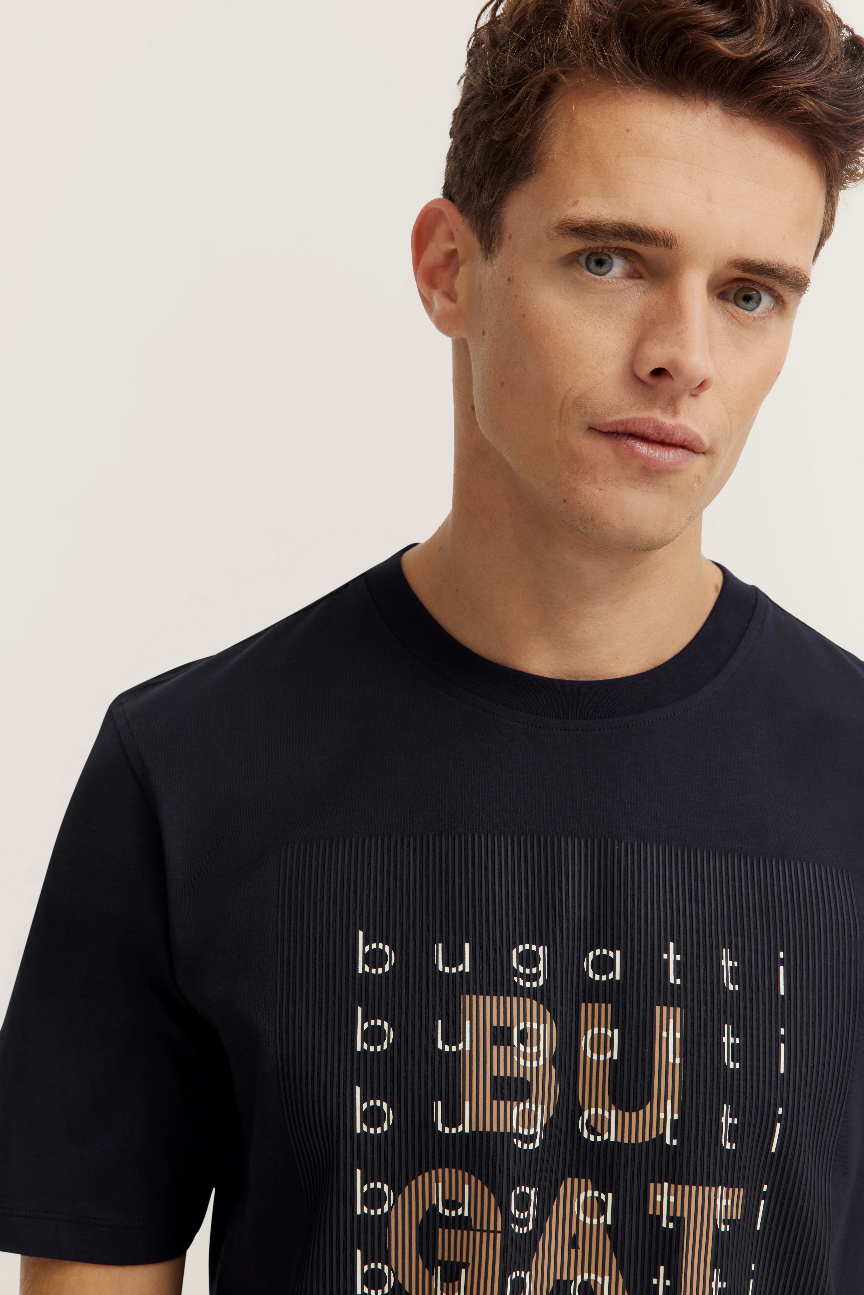 Model in schwarzem bugatti T-Shirt mit Logo-Print, Büstenbild, entspanntes Posing.