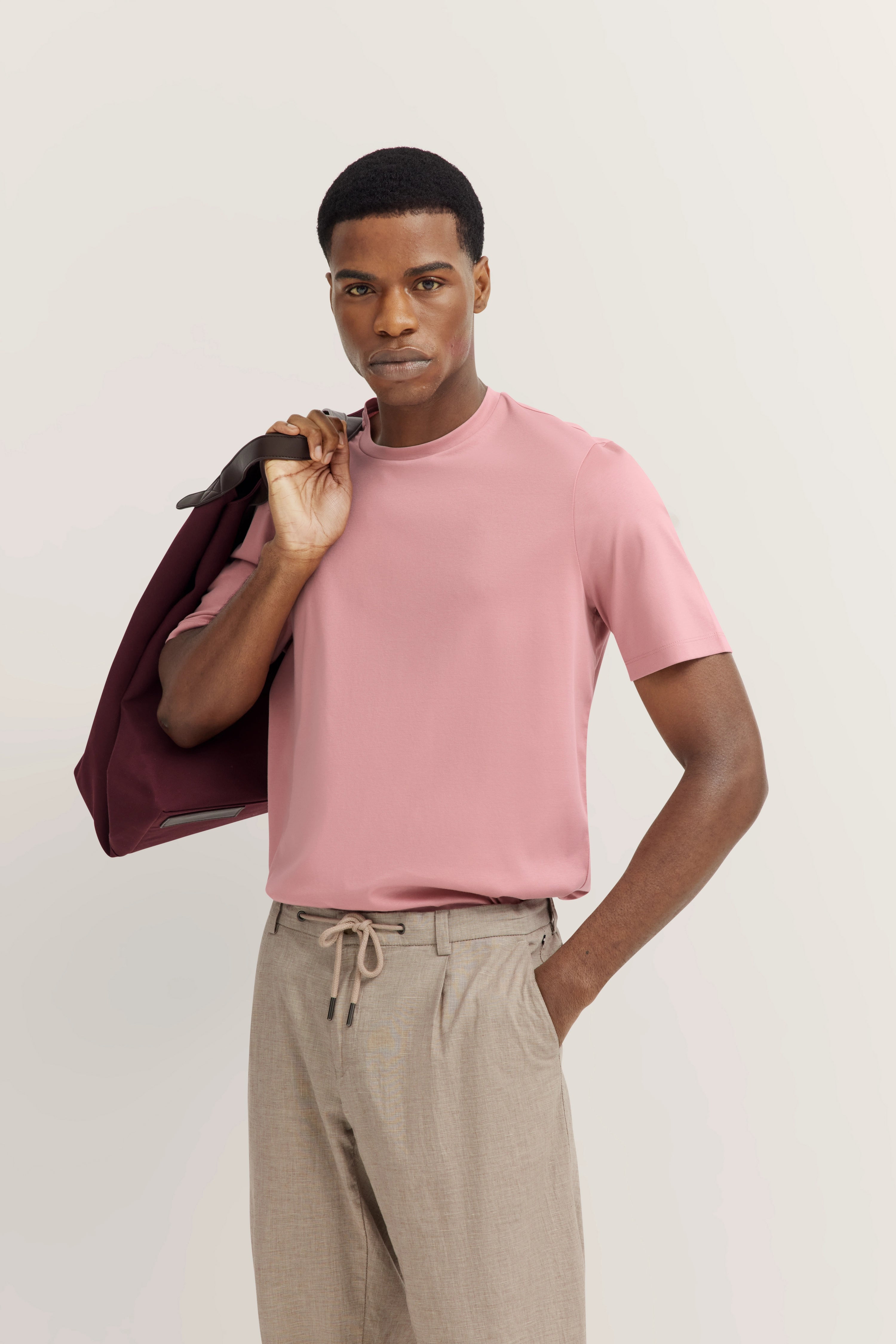 Model in pink bugatti T-shirt, beige pants, holding maroon blazer over shoulder, casual pose.