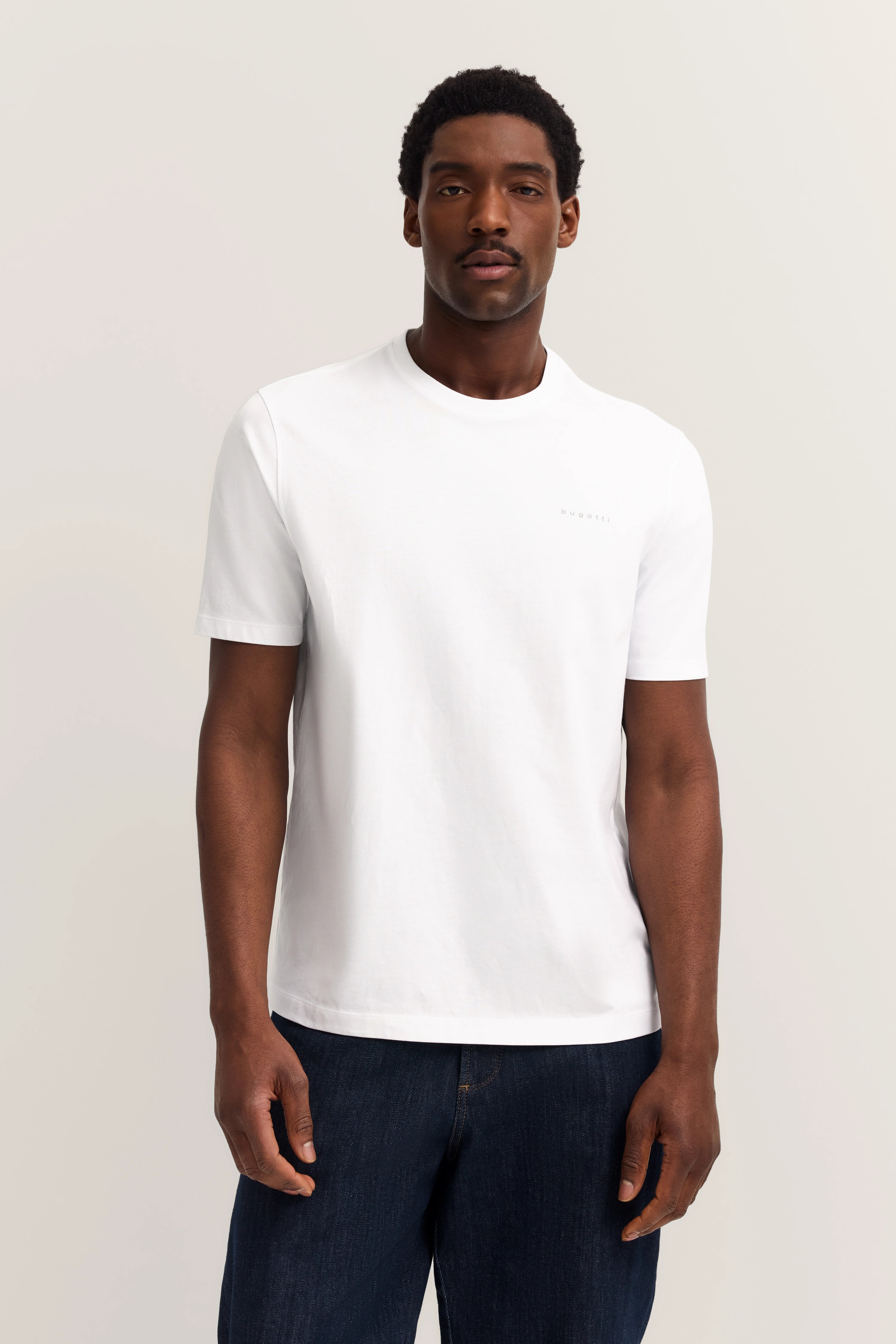 Weißes bugatti T-Shirt, Modellbild, entspannte Pose, kombiniert mit dunklen Jeans.