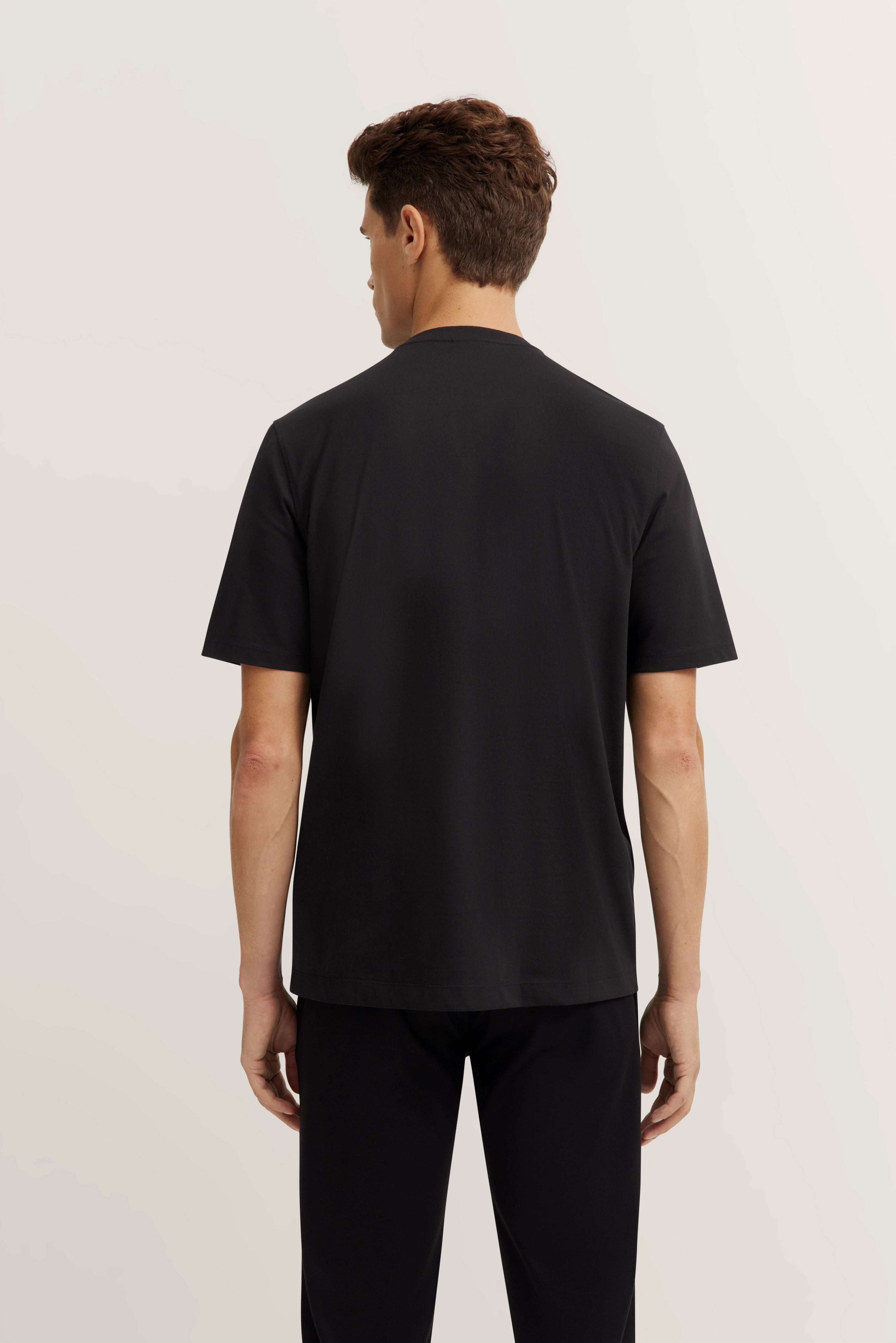 Back view of model in black bugatti T-shirt and pants, standing casually.