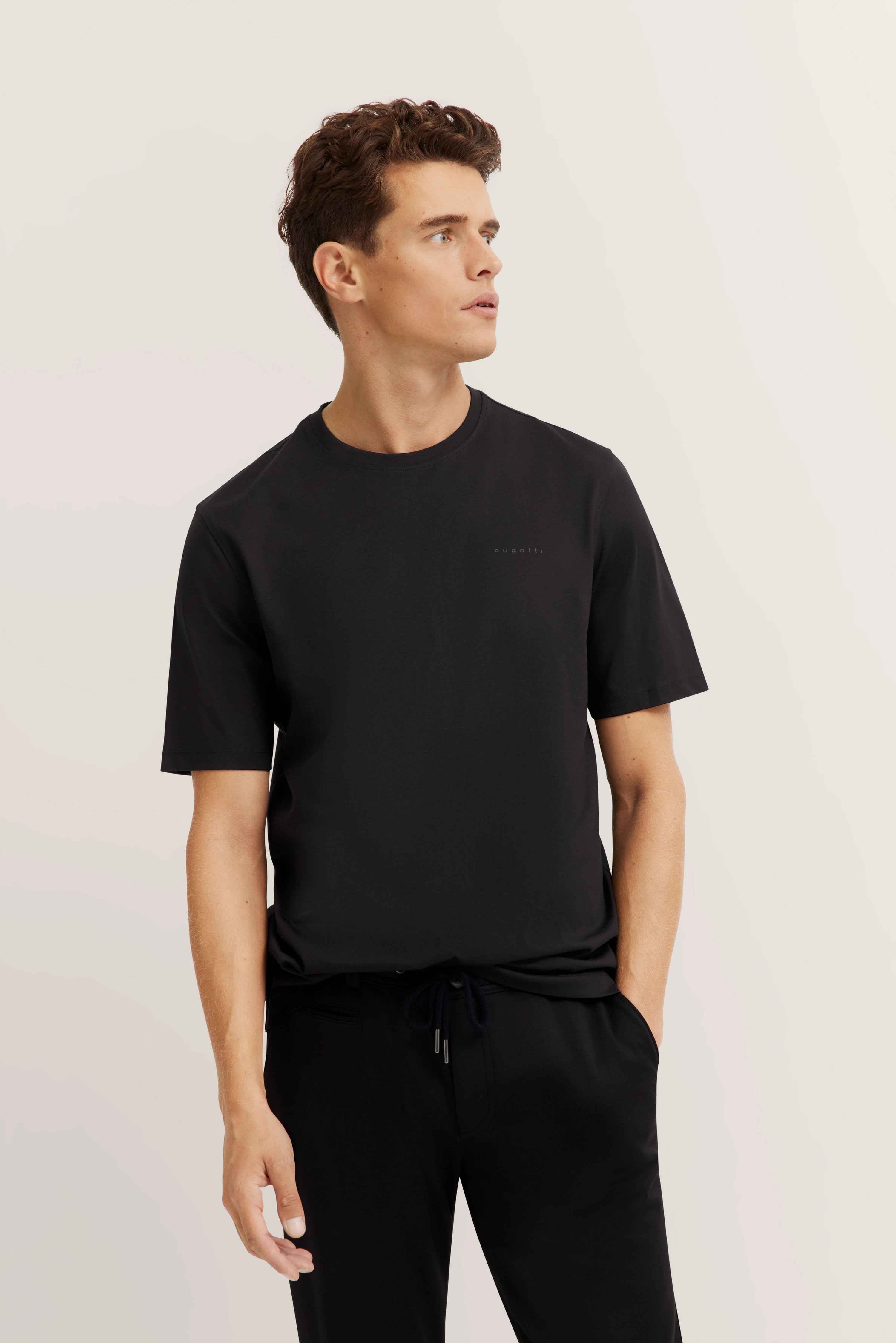 Model in black bugatti T-shirt and pants, casual pose, looking left.