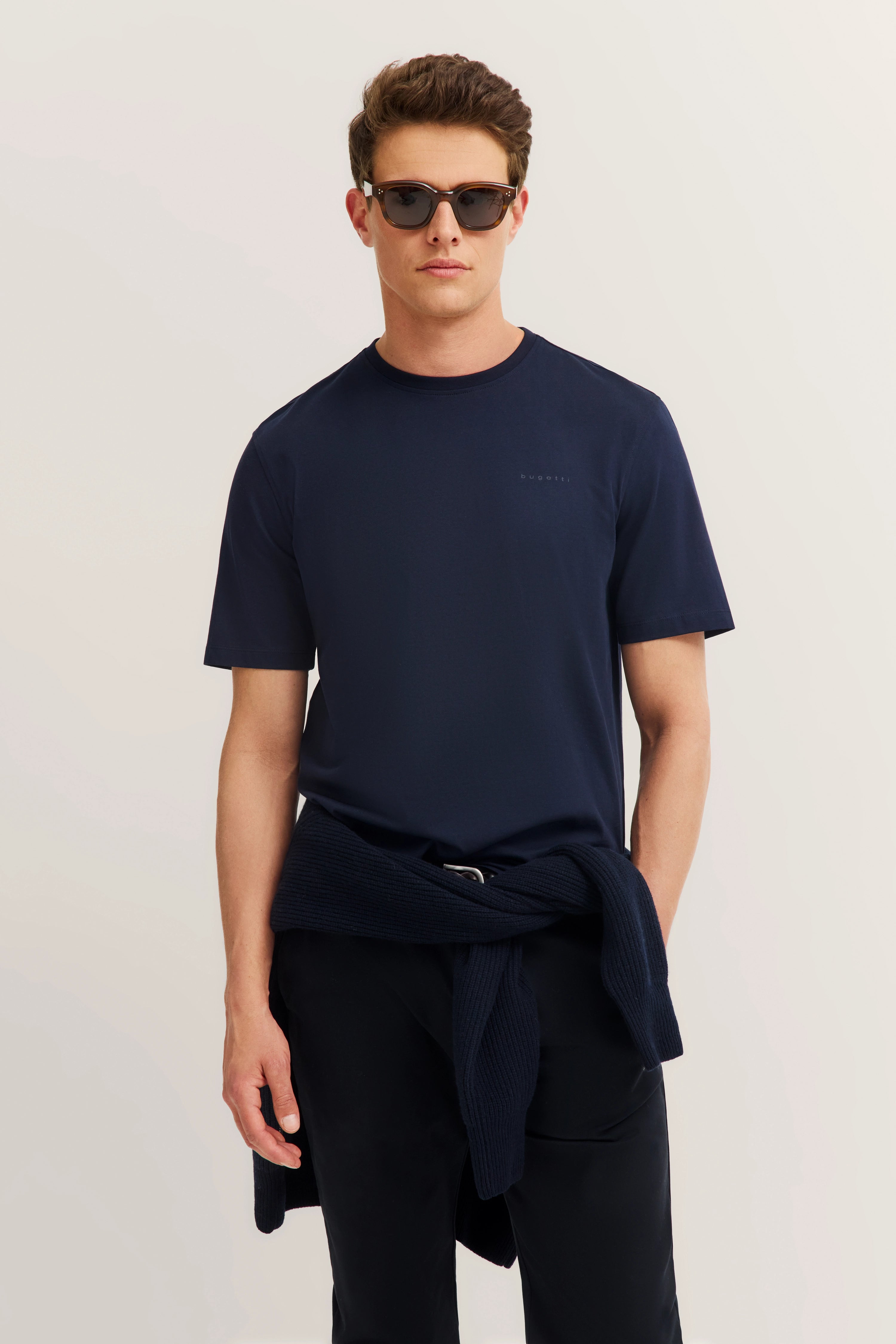 Model in navy bugatti T-Shirt und Hose, Pullover um die Taille, lässige Pose.
