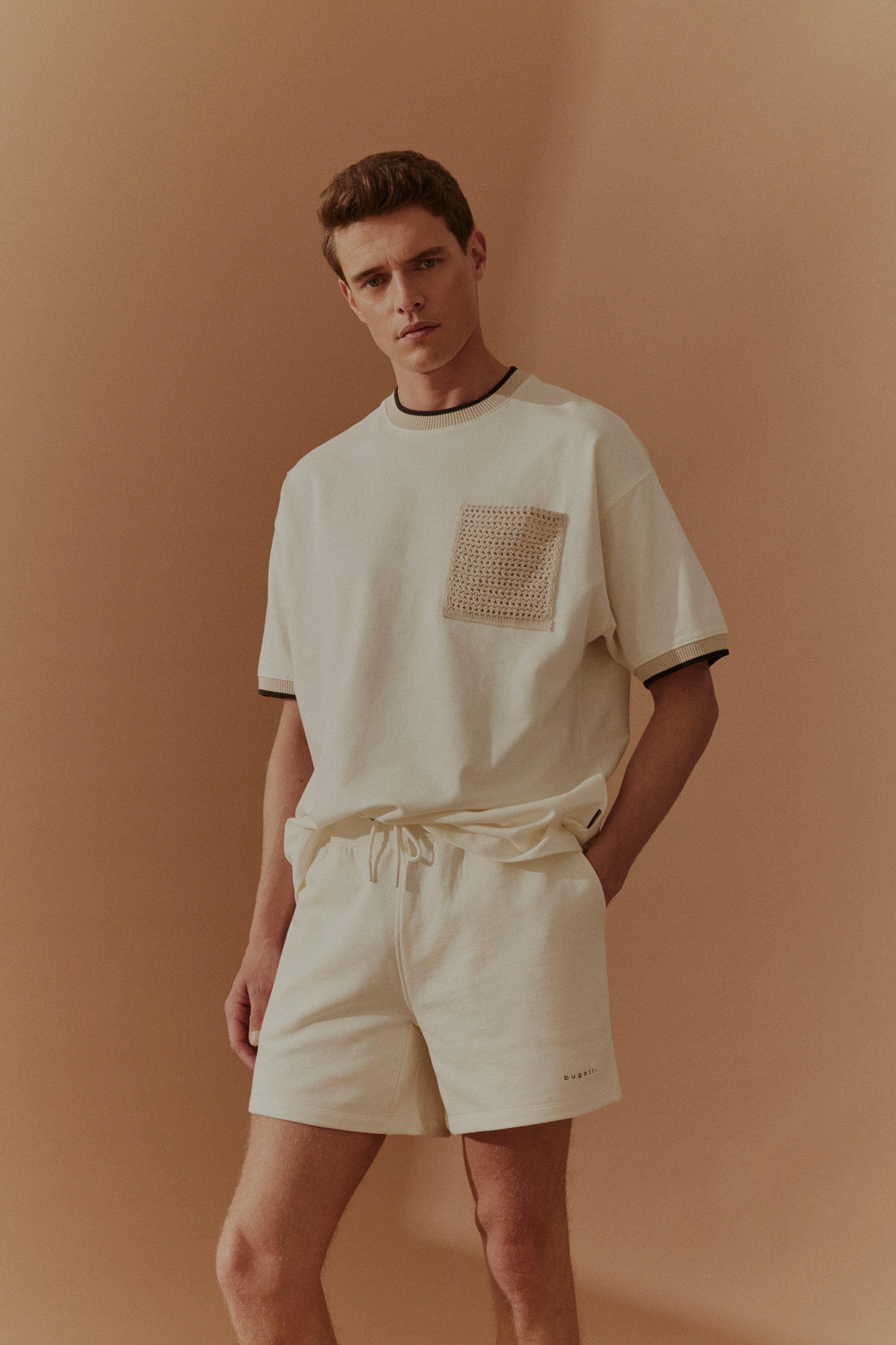 Helles bugatti Outfit mit T-Shirt und Shorts, Model stehend, entspannte Pose.