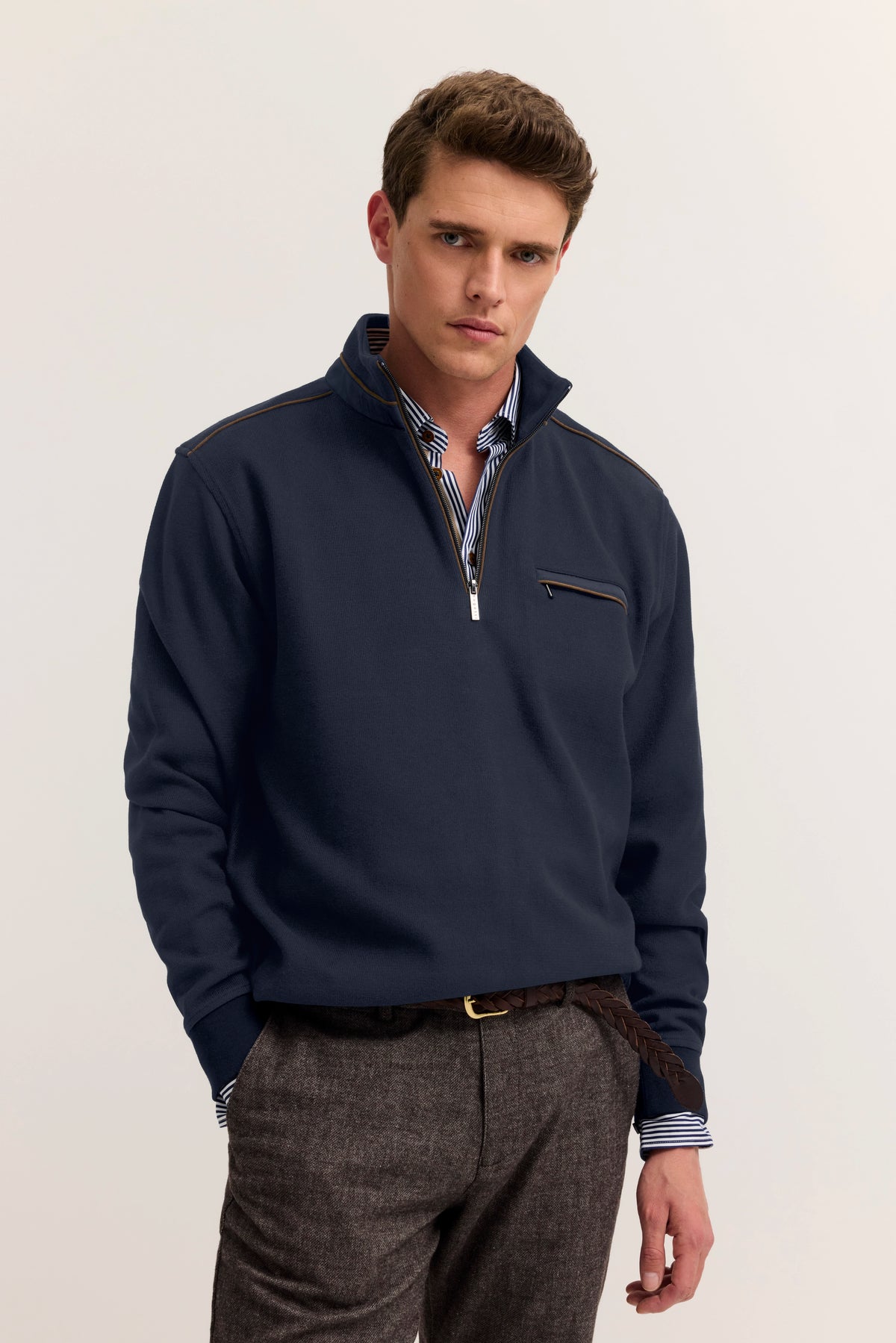 bugatti Model in blauem Pullover mit Reißverschluss, gestreiftem Hemd, grauer Hose, legeres Posing.