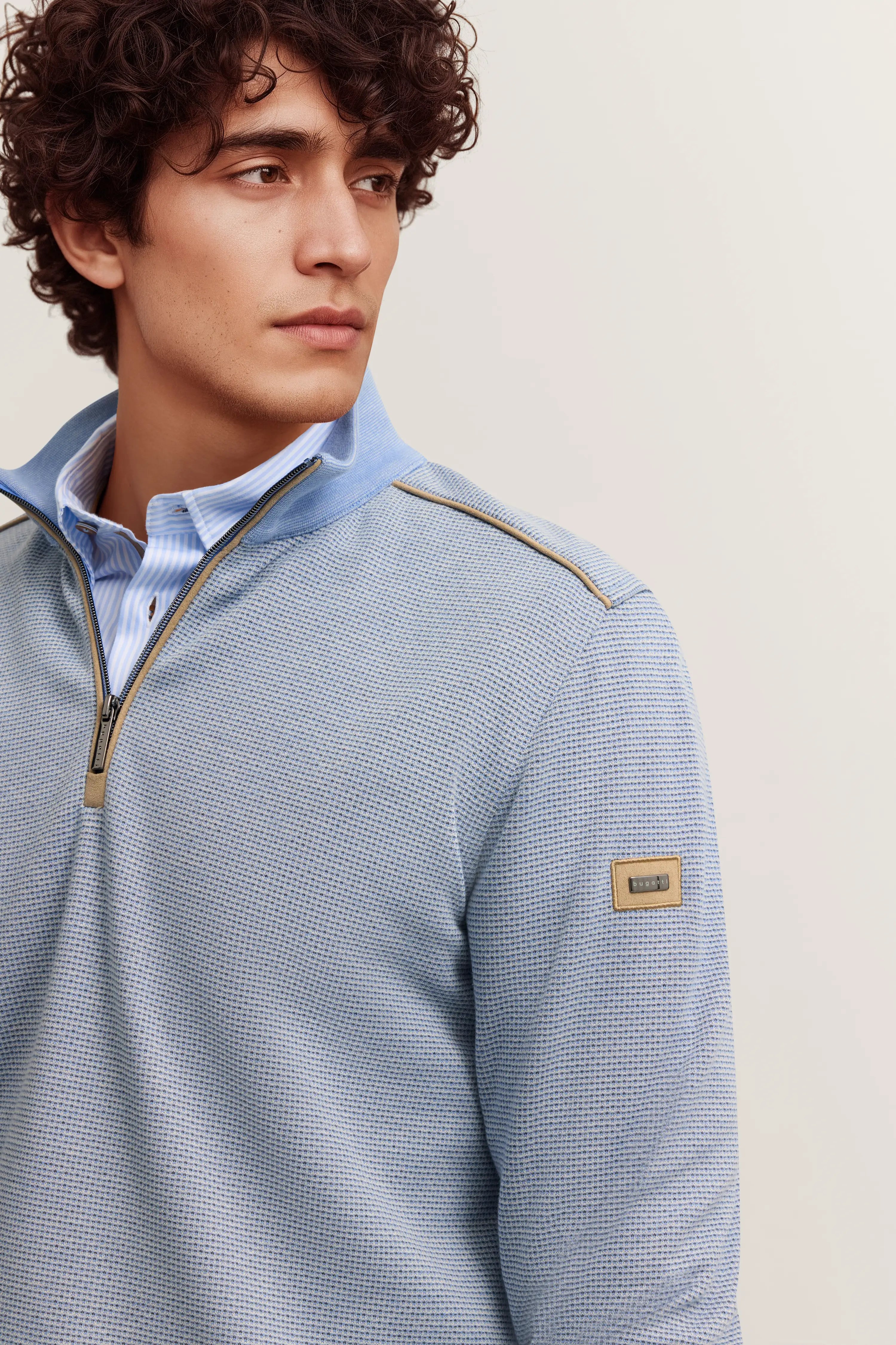 Bugatti Modelbild mit blauem Pullover und Hemd, elegantes Posing, stilvoll und zeitlos.