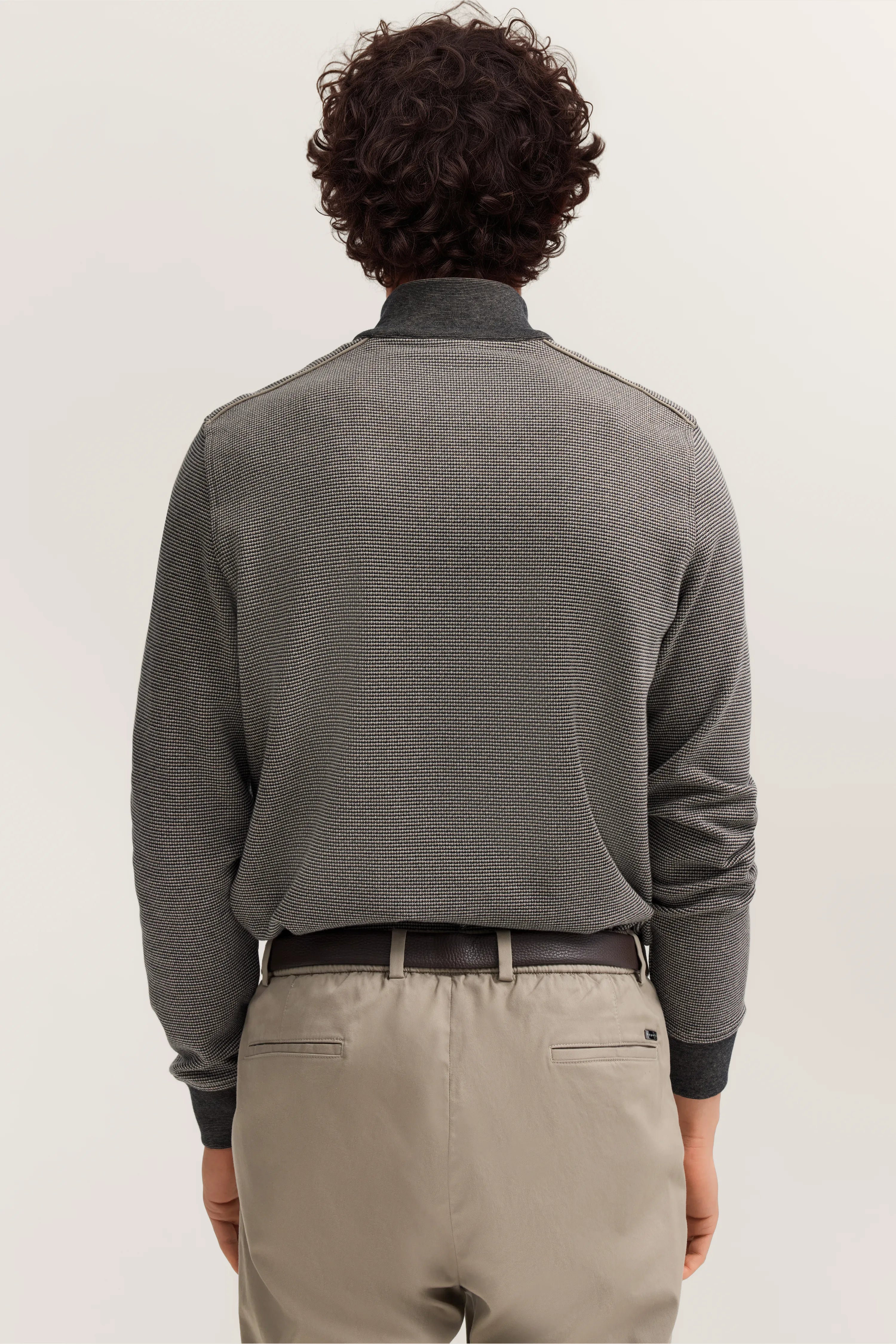 Grauer Pullover und beige Hose von hinten, legeres Modelbild, entspannter Stand.