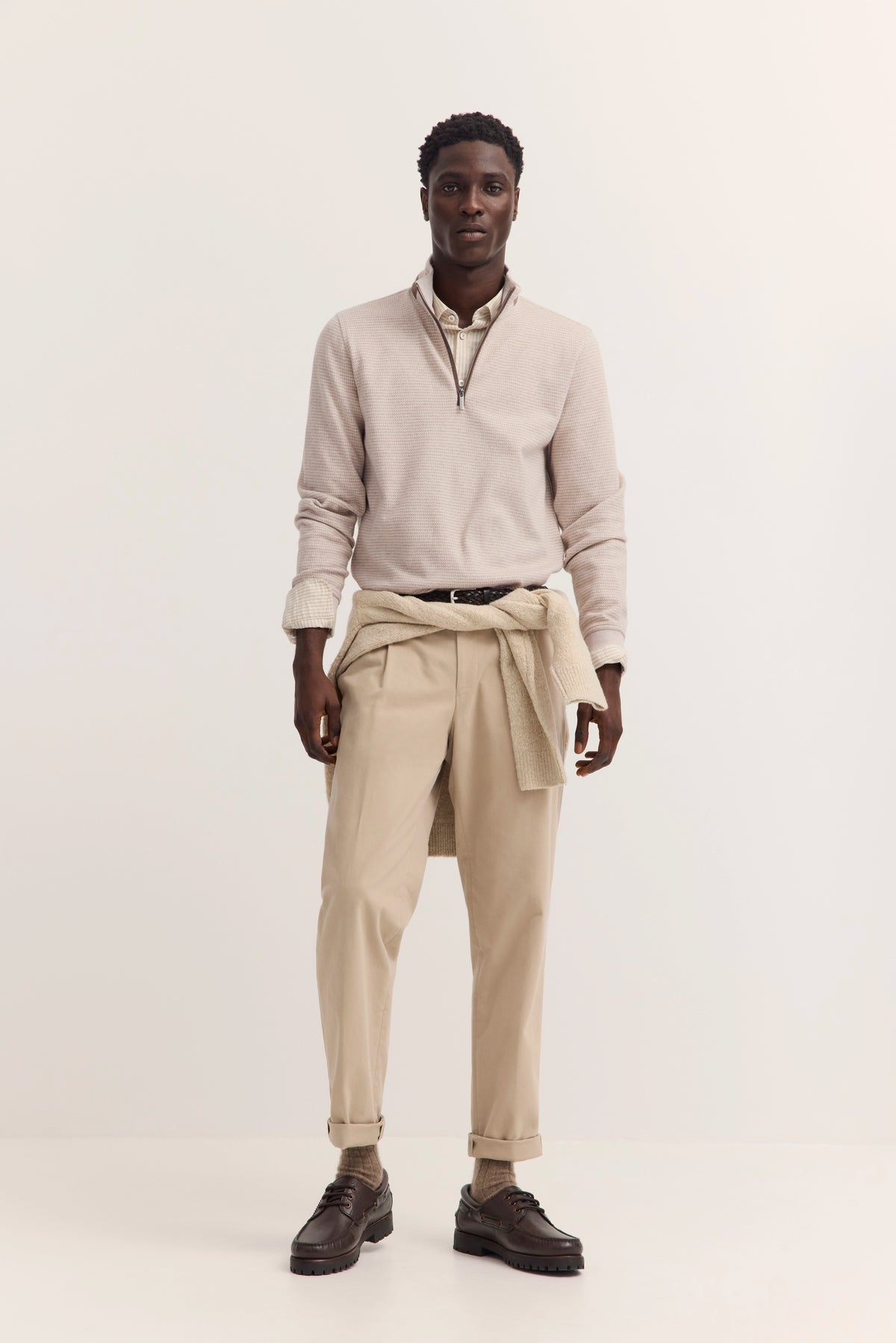bugatti Model in beige Pullover, heller Hose, Pullover um Hüfte, lässig stehend.