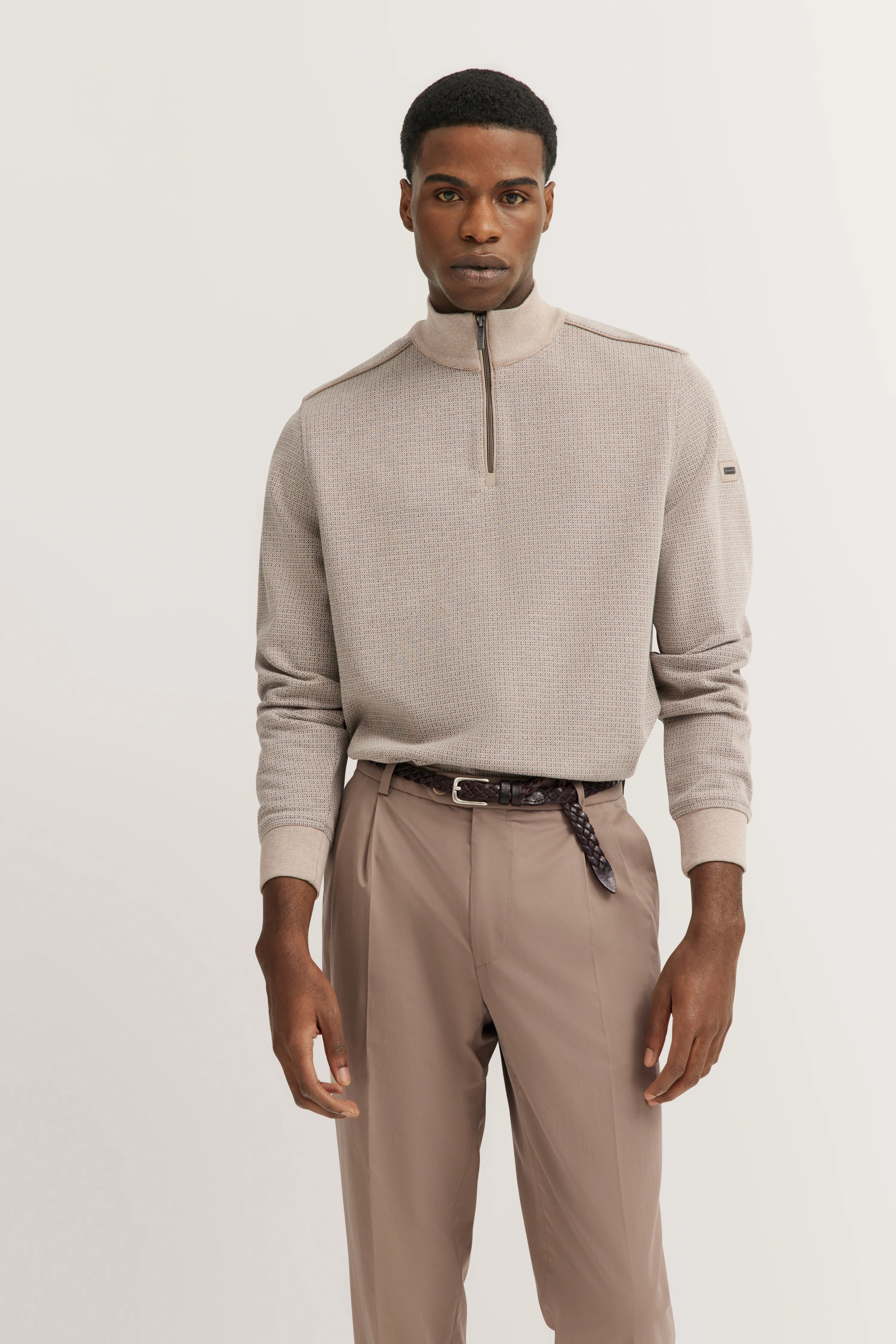 Model in beigefarbenem bugatti-Pullover mit Reißverschluss und beigen Hosen, lässige Pose.