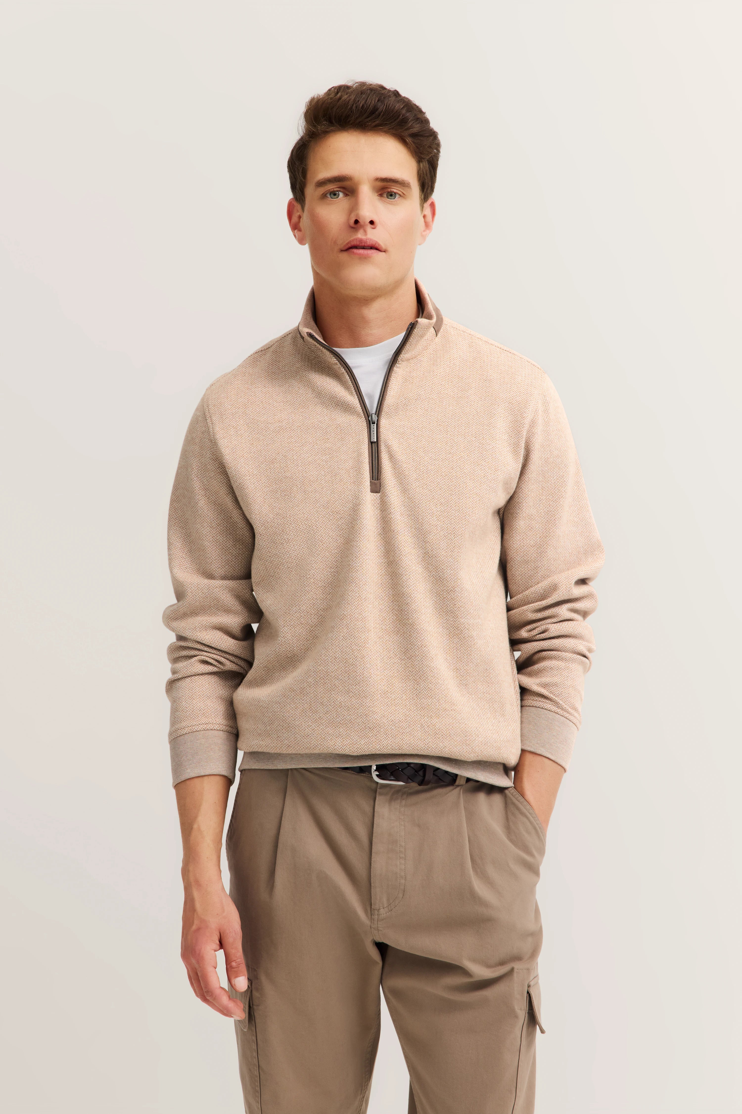 Beigefarbener Pullover mit Reißverschluss und hellbrauner Hose, Model posiert lässig, bugatti Stil.