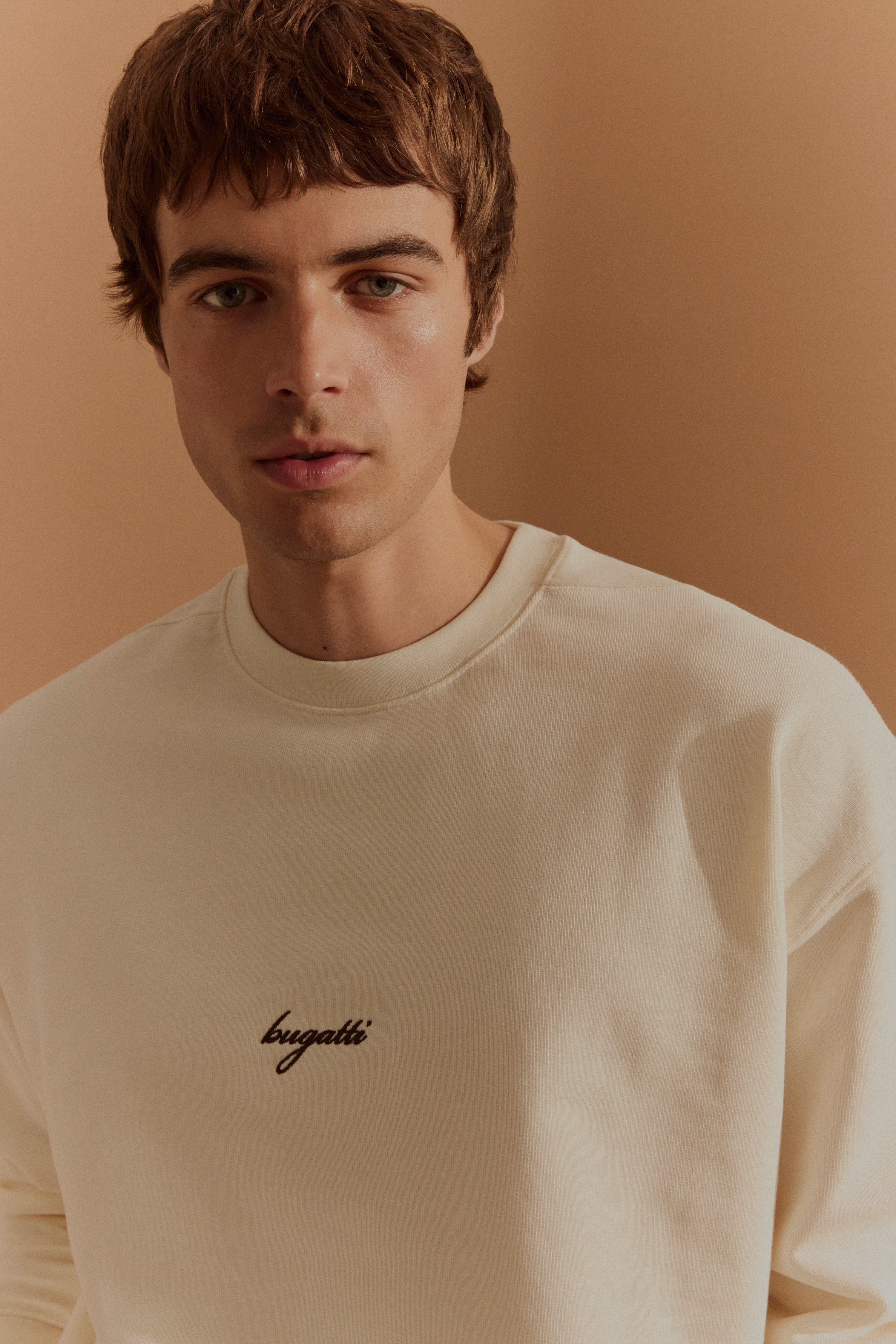 Alt-Text: Model in cremefarbenem bugatti Sweatshirt, legerer Stil, neutraler Hintergrund.