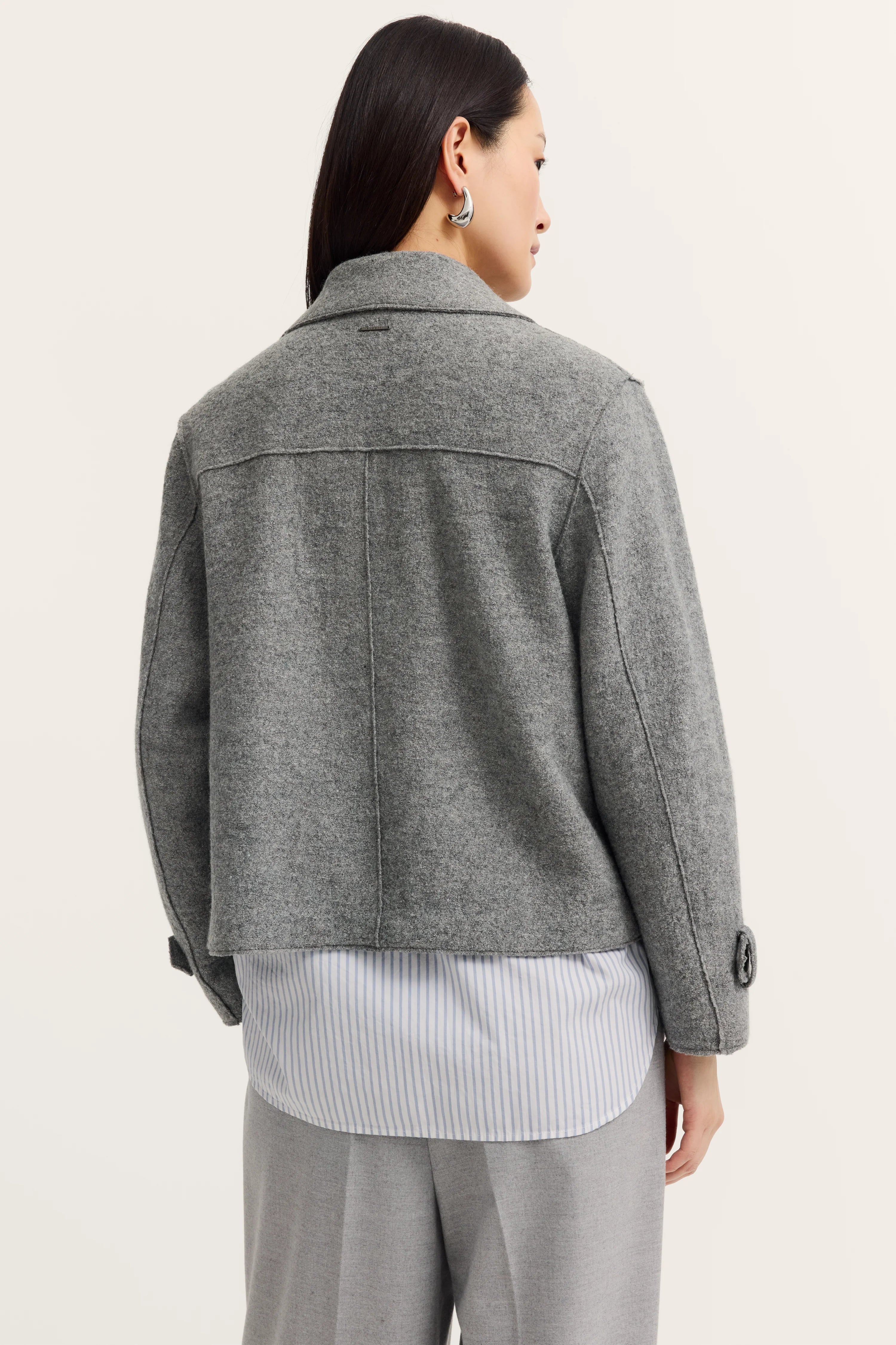 Graue Jacke über gestreiftem Hemd, graue Hose, Model von hinten, entspannte Pose.