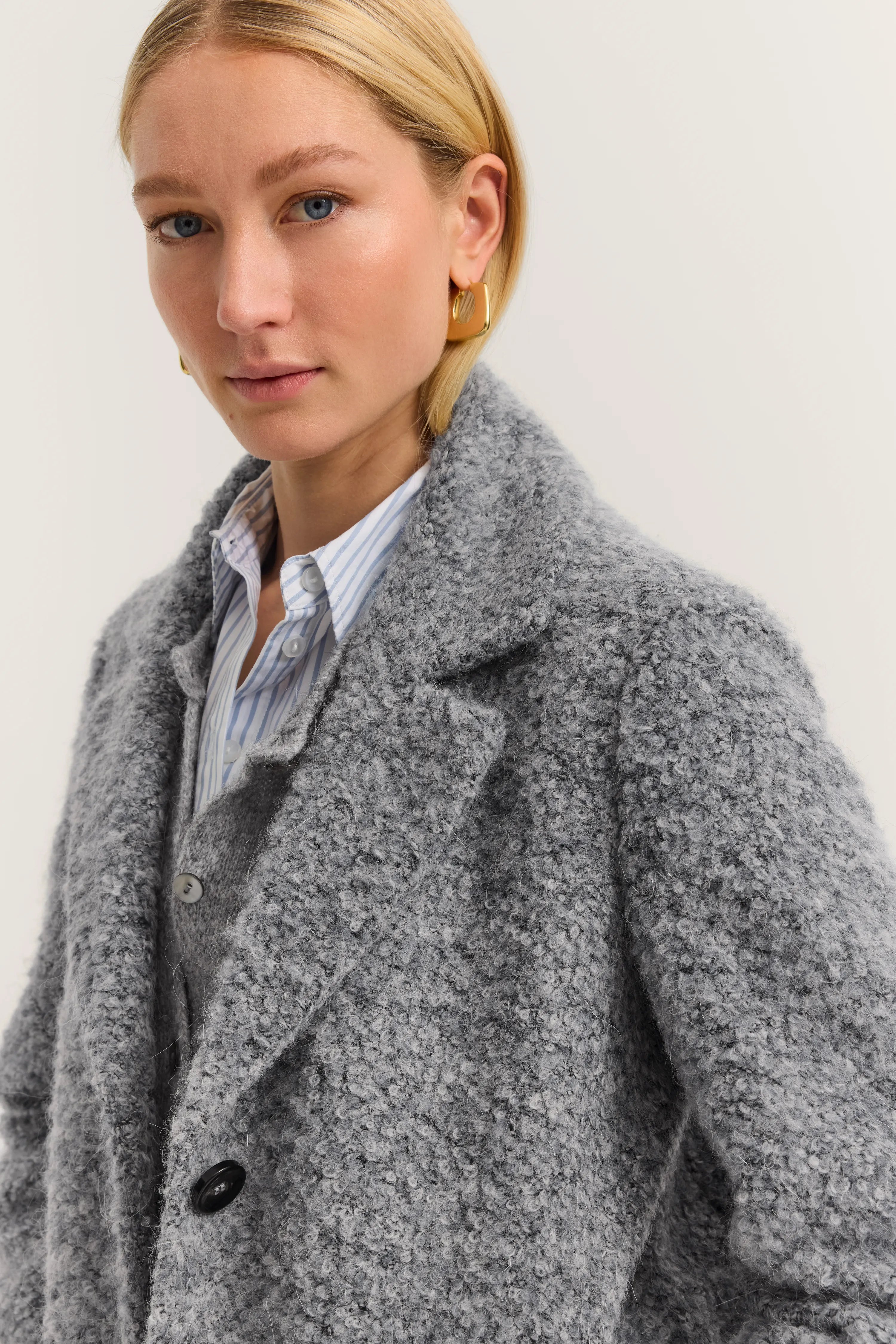 Grauer Bouclé-Mantel, gestreifte Bluse, Modelbild, entspannter Gesichtsausdruck, bugatti Stil.