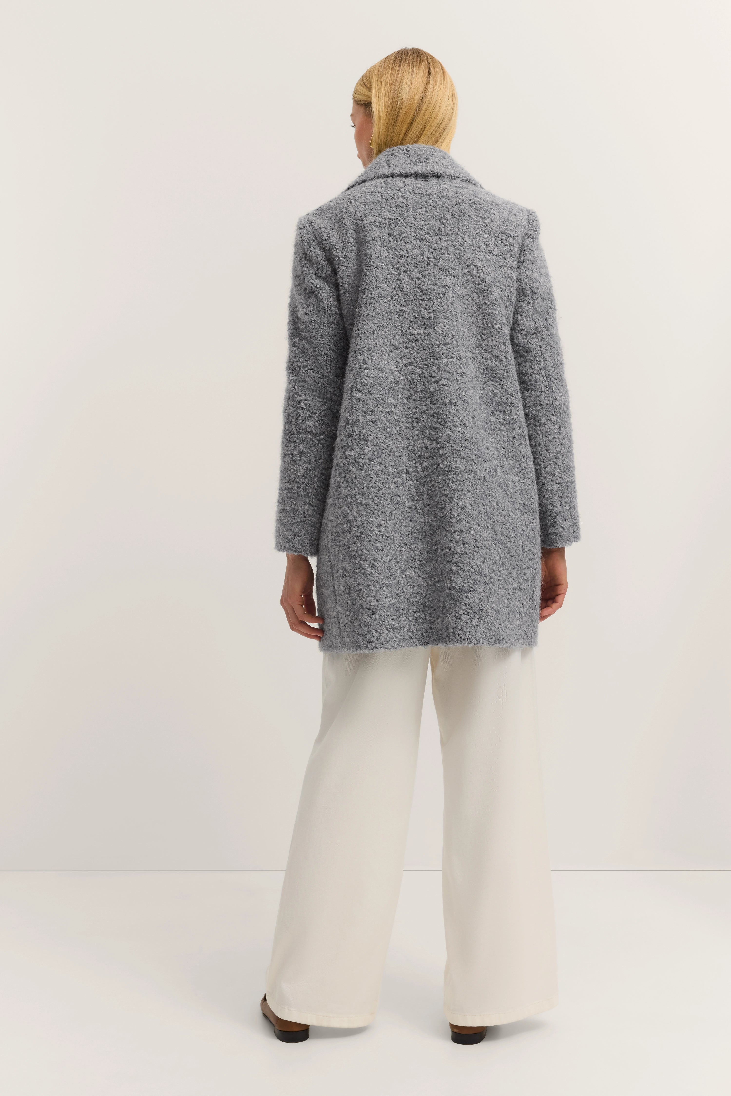 Grauer bugatti Mantel mit weißer Hose, Model von hinten, entspannt stehend.