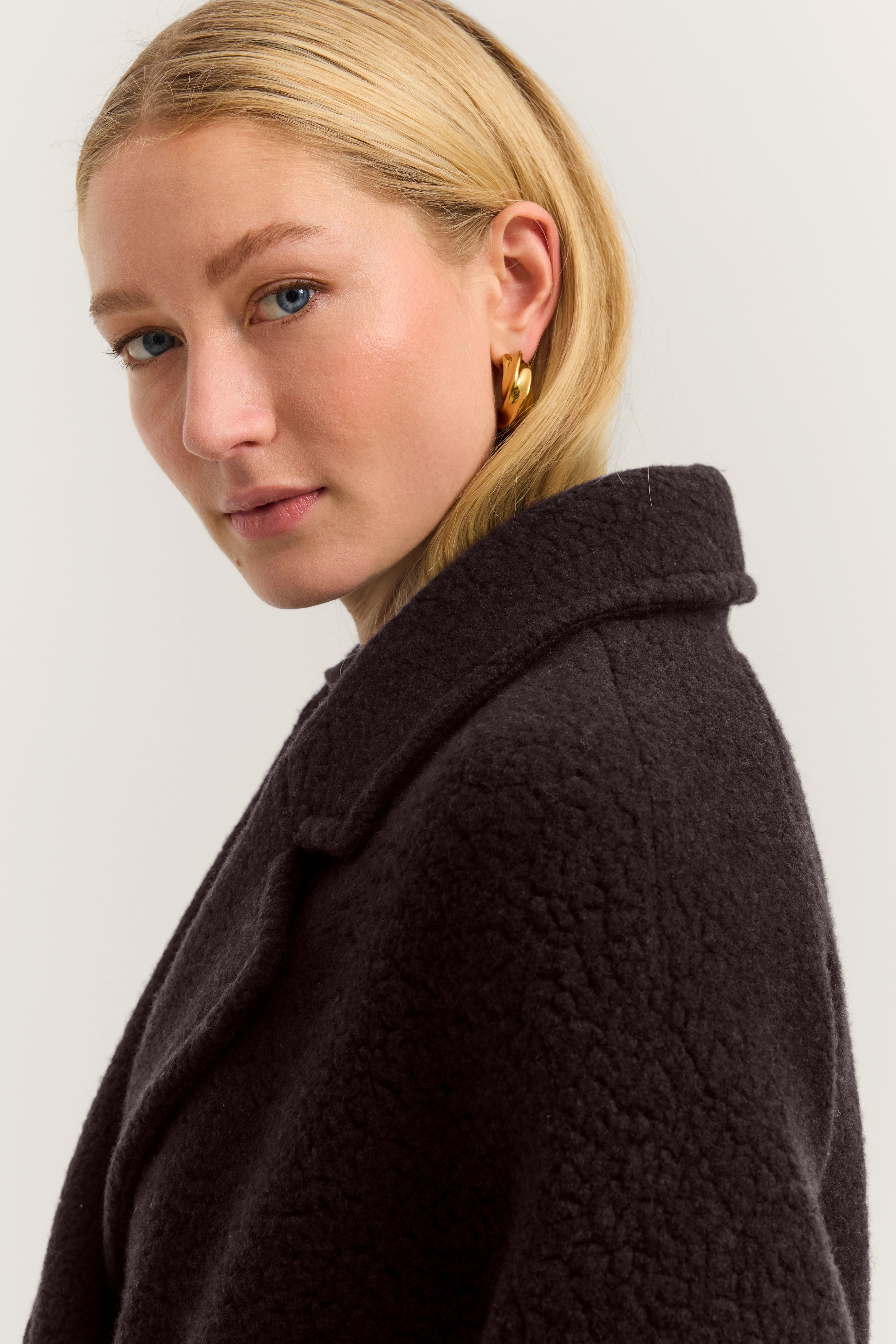 Büstenbild mit schwarzem bugatti Mantel, Modell mit goldenen Ohrringen, eleganter Look.