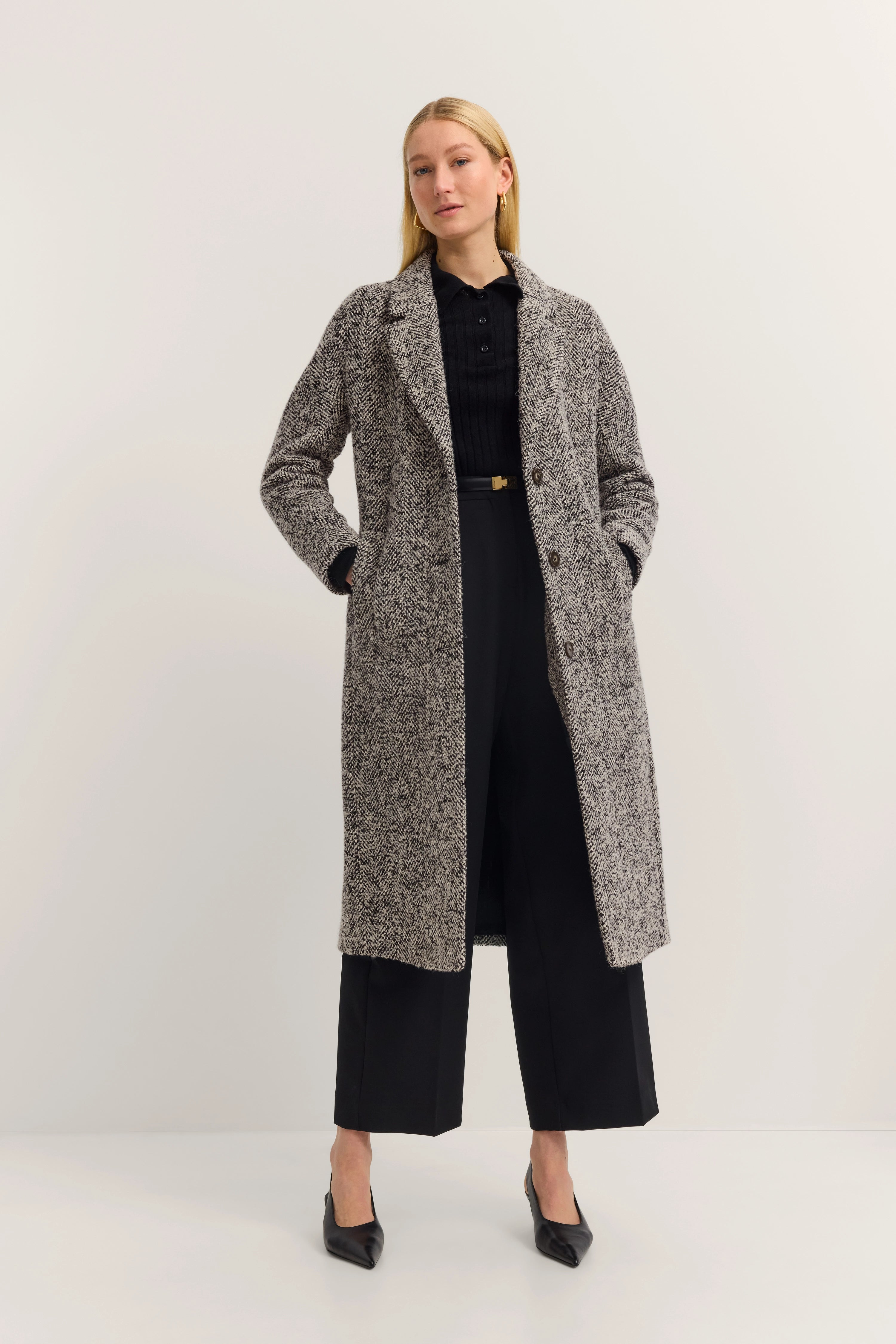 Grauer Tweed-Mantel über schwarzer Bluse und Hose, Modelbild, entspannte Haltung.