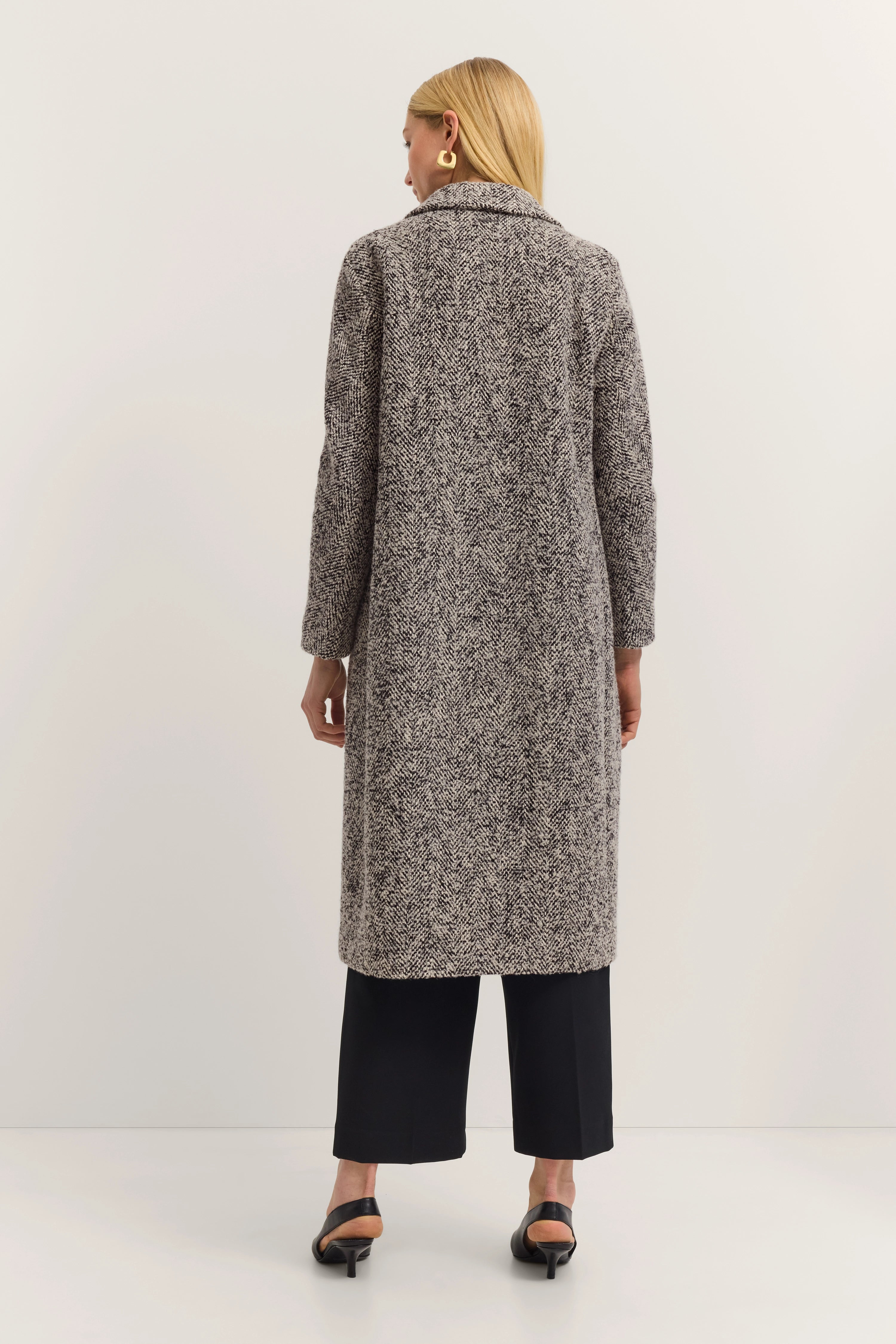 Grauer Mantel mit Fischgrätmuster, Model von hinten, schwarze Hose, entspanntes Posing.