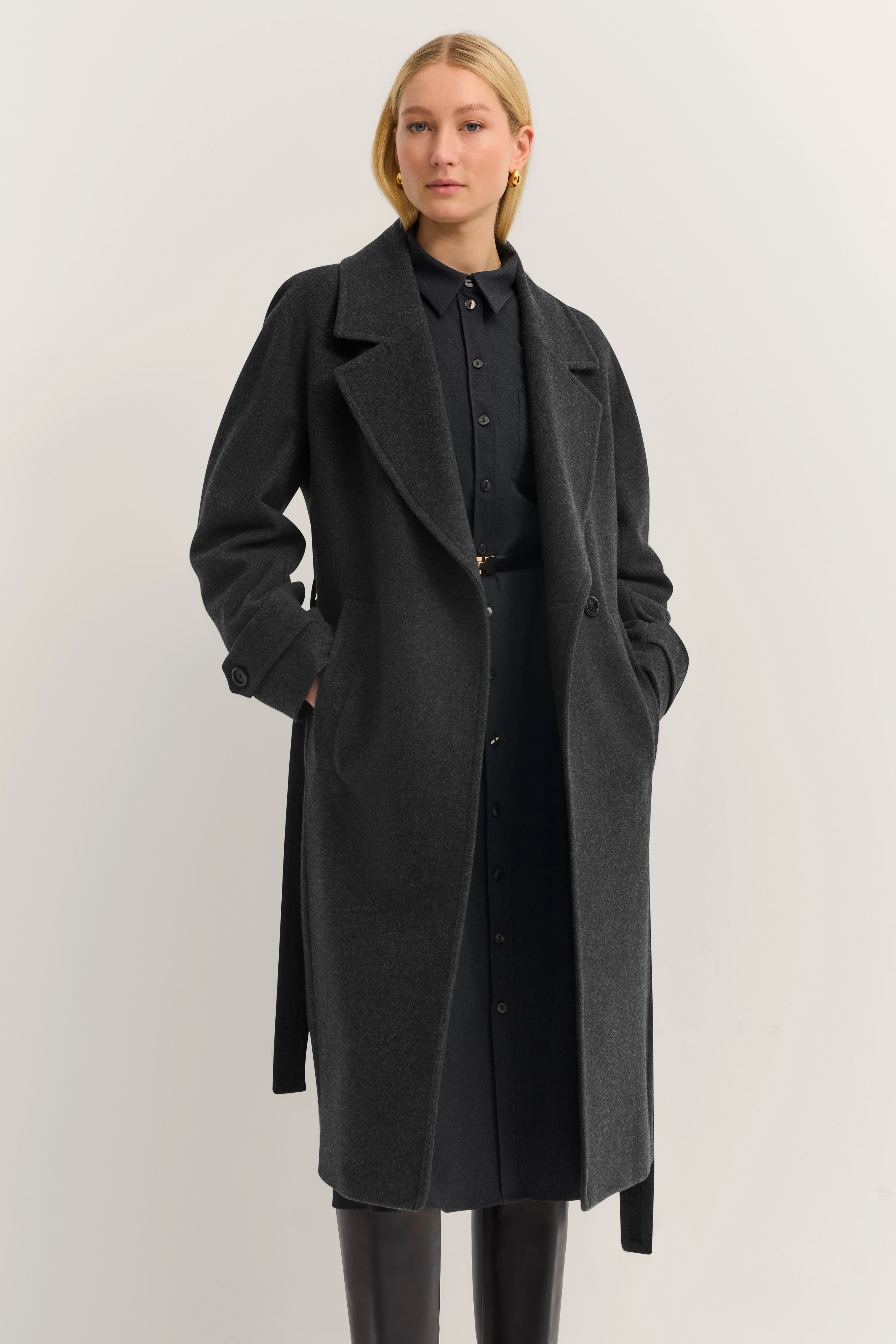 Grauer bugatti Mantel über schwarzem Hemdkleid, Model posiert mit Händen in den Taschen.