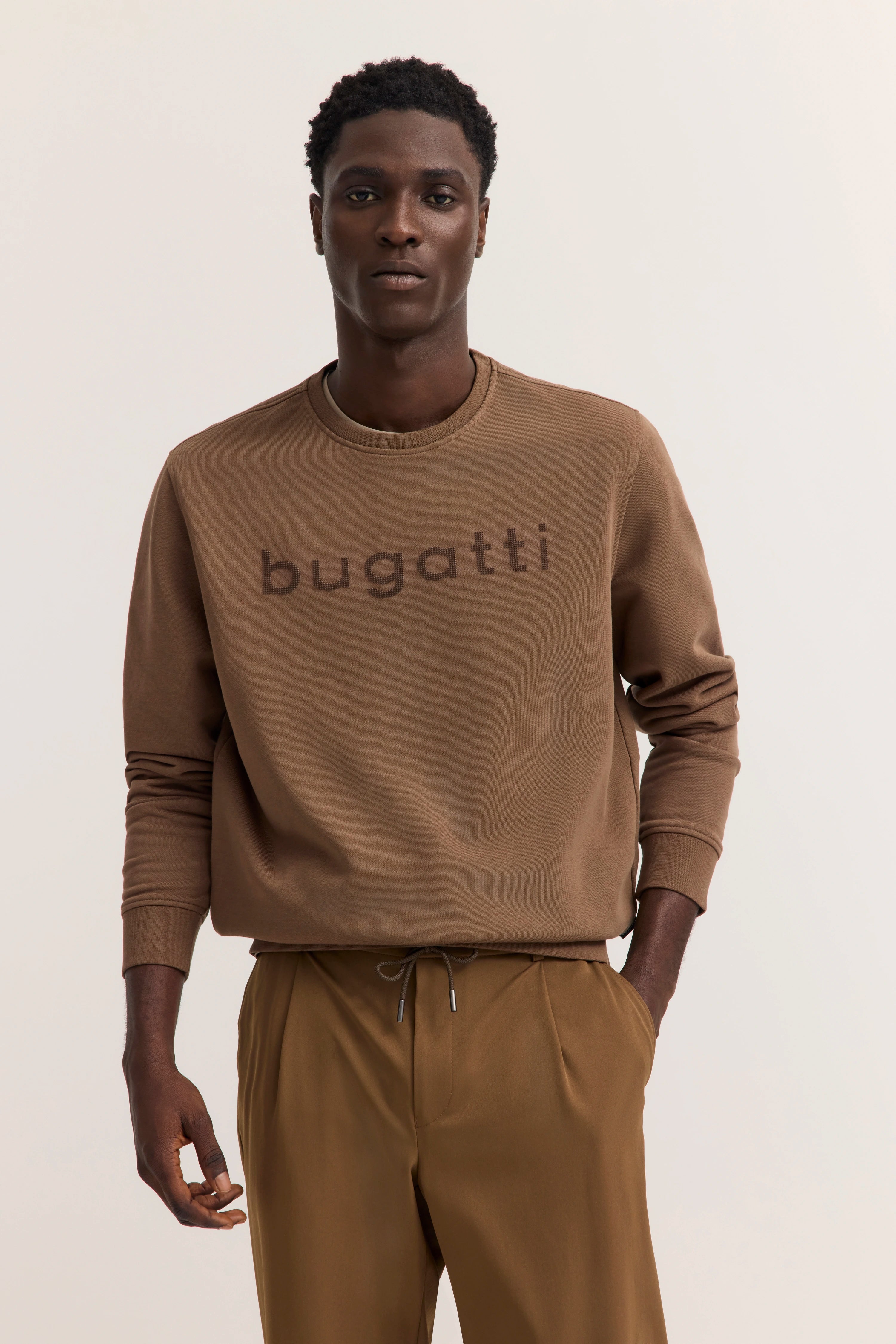 Model trägt braunen bugatti Pullover und Hose, entspannte Pose.