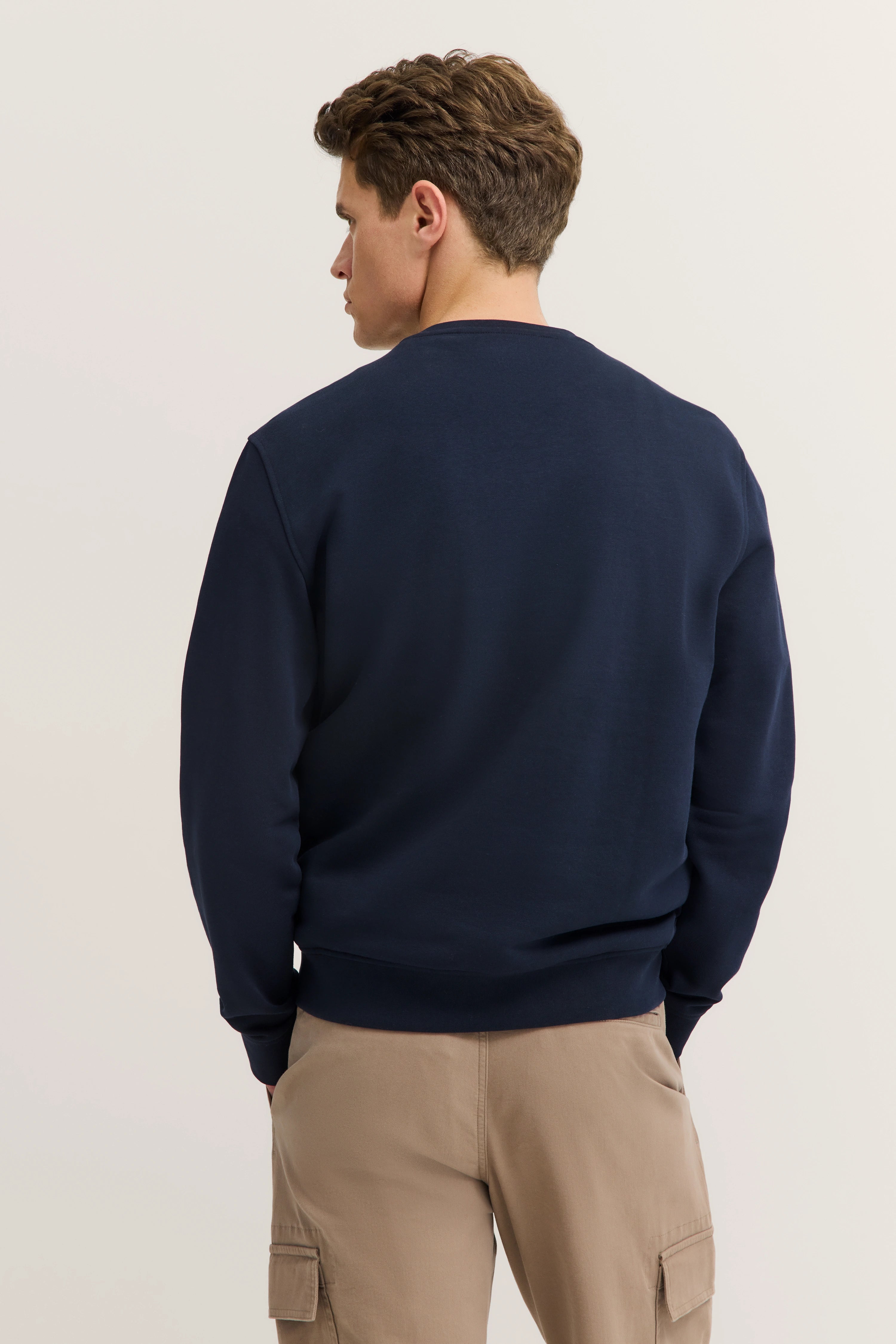 Navy Pullover mit beige Cargohose, Model von hinten, entspannte Pose, bugatti.
