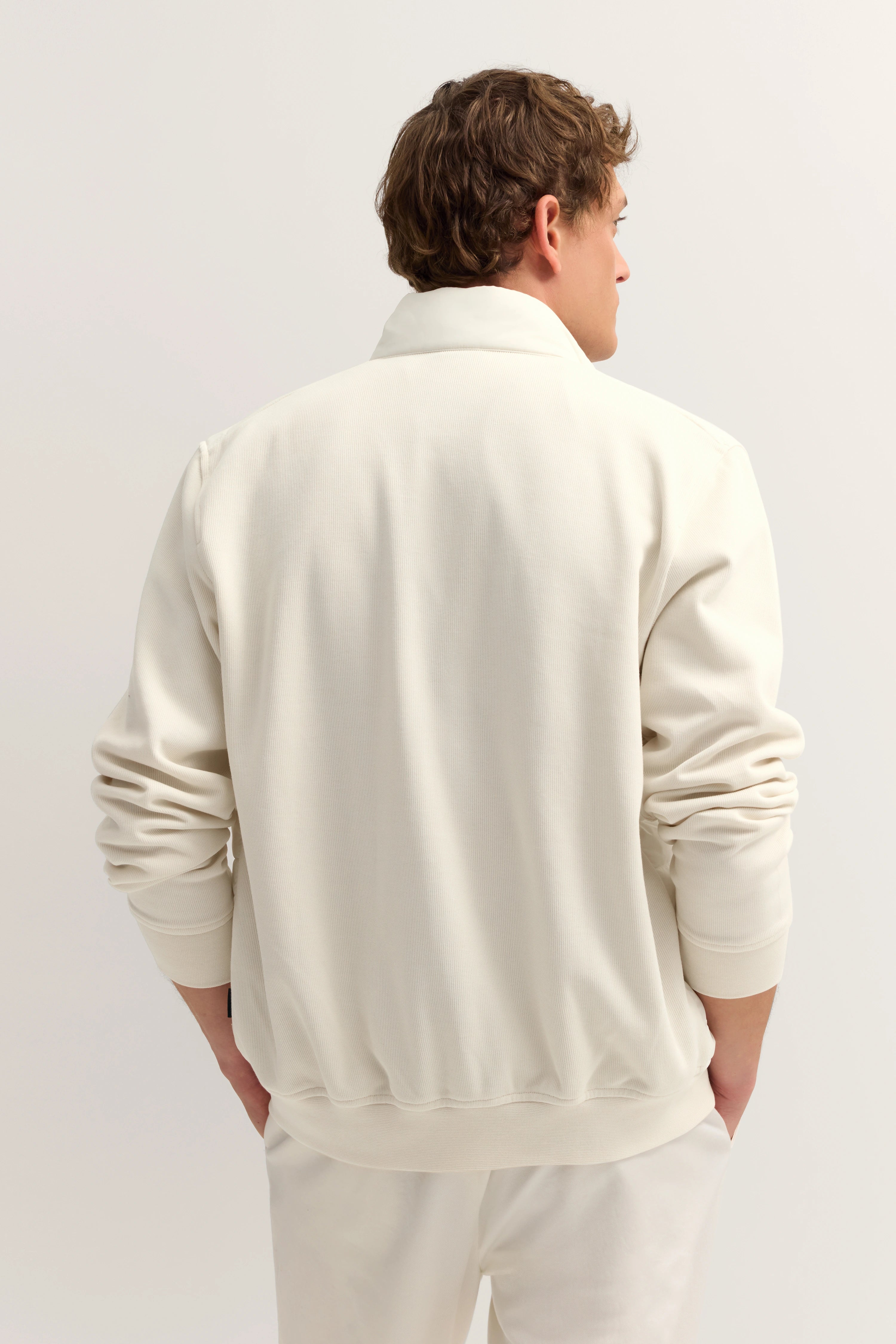 Herrenmodel in cremefarbenem bugatti-Leger-Outfit, Rückenansicht, Hände in Taschen.