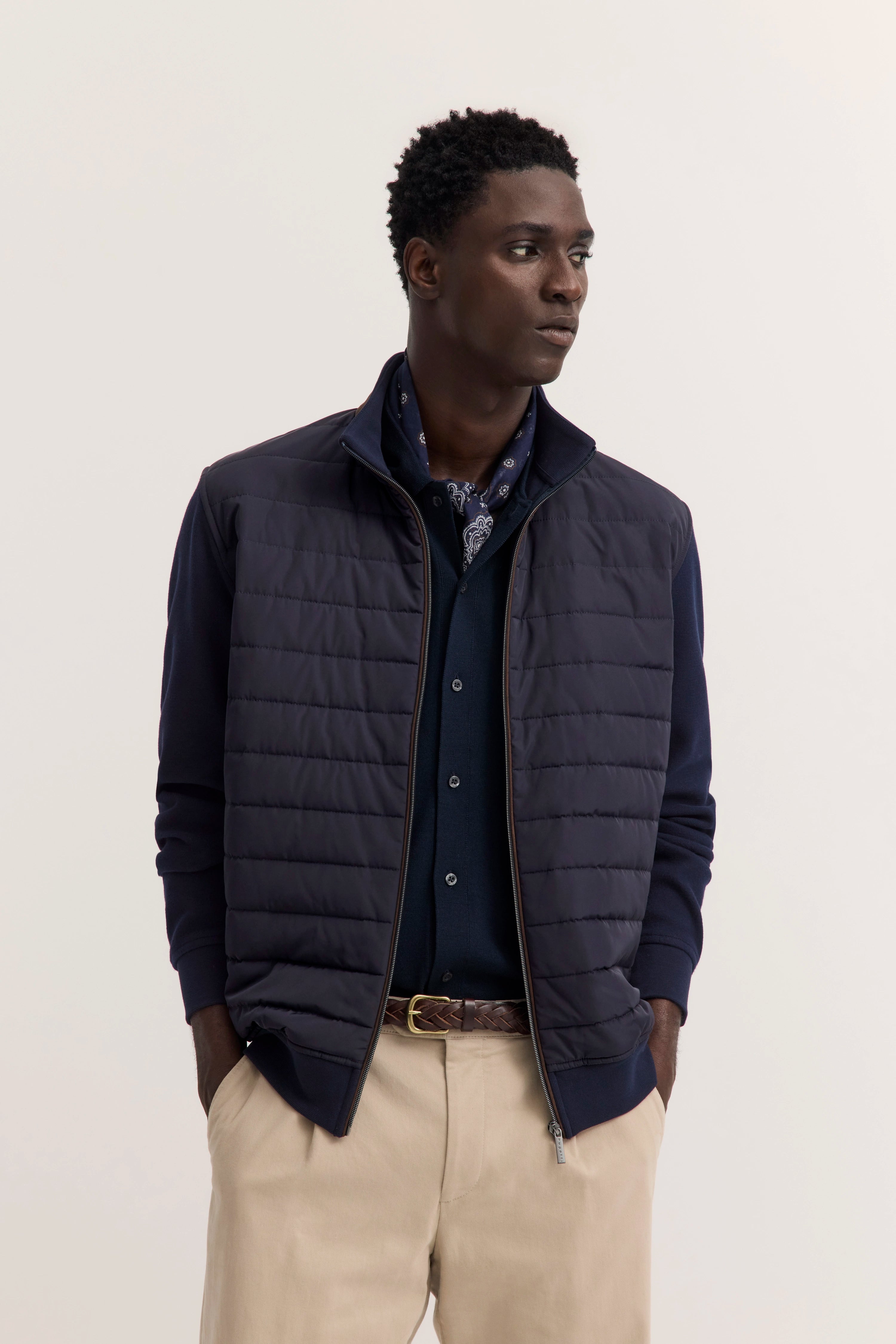 Model in navy Steppweste, Hemd und beiger Hose von bugatti, lässiges Posing.