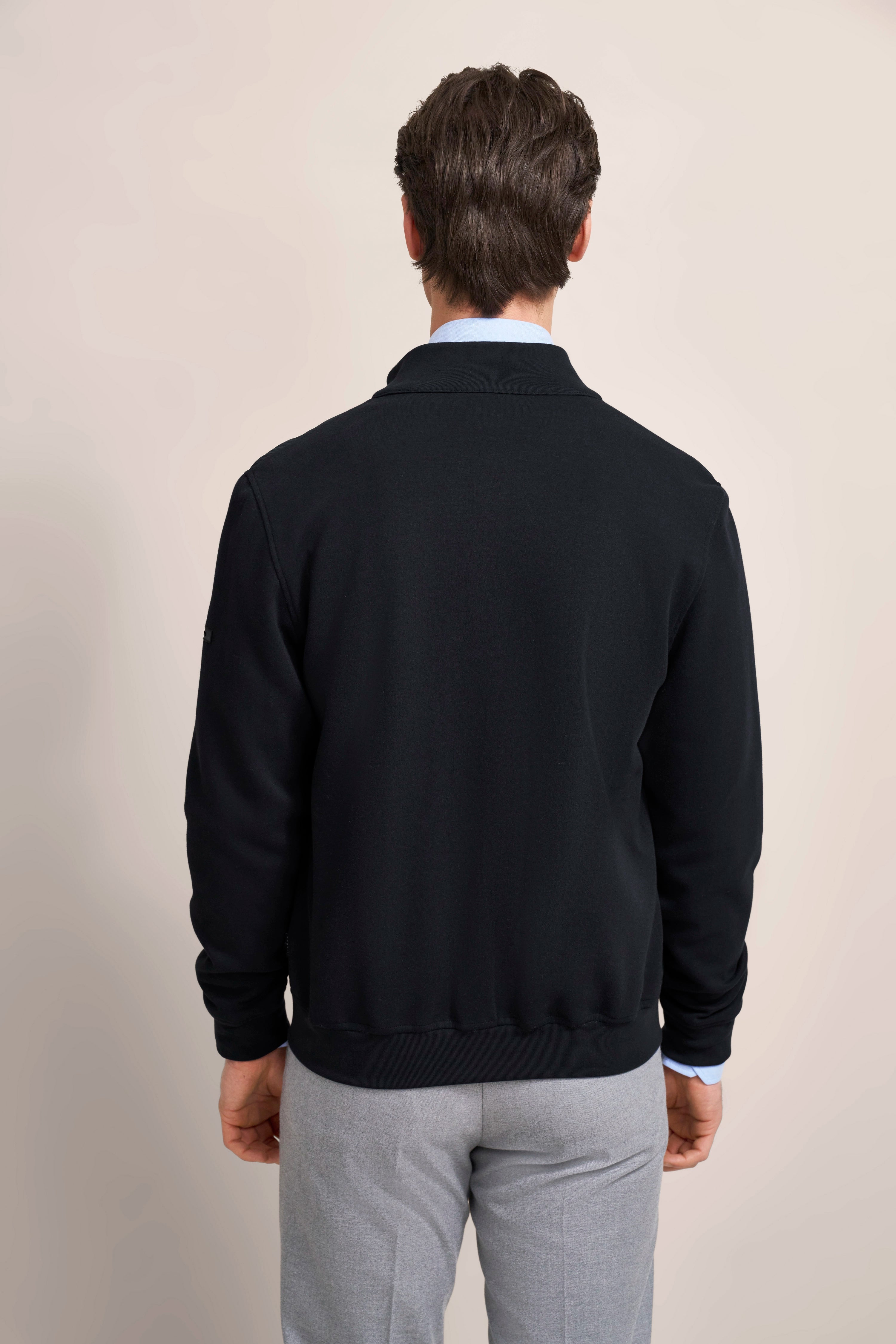 bugatti Modelbild, Rückenansicht, schwarzer Pullover, graue Hose, entspanntes Posing.