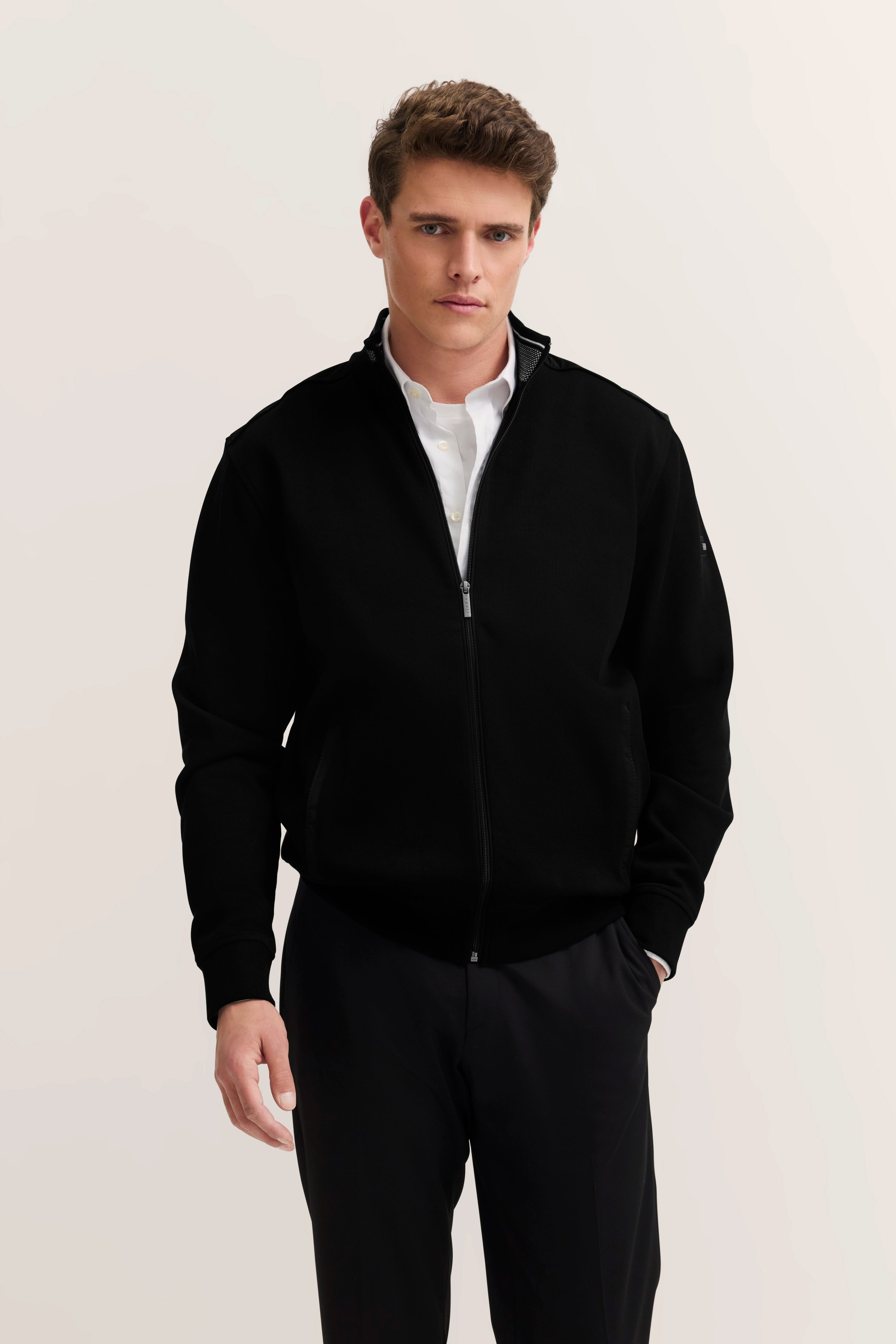 bugatti Modelbild: Mann in schwarzer Jacke, weißem Hemd, schwarze Hose, lässige Pose.
