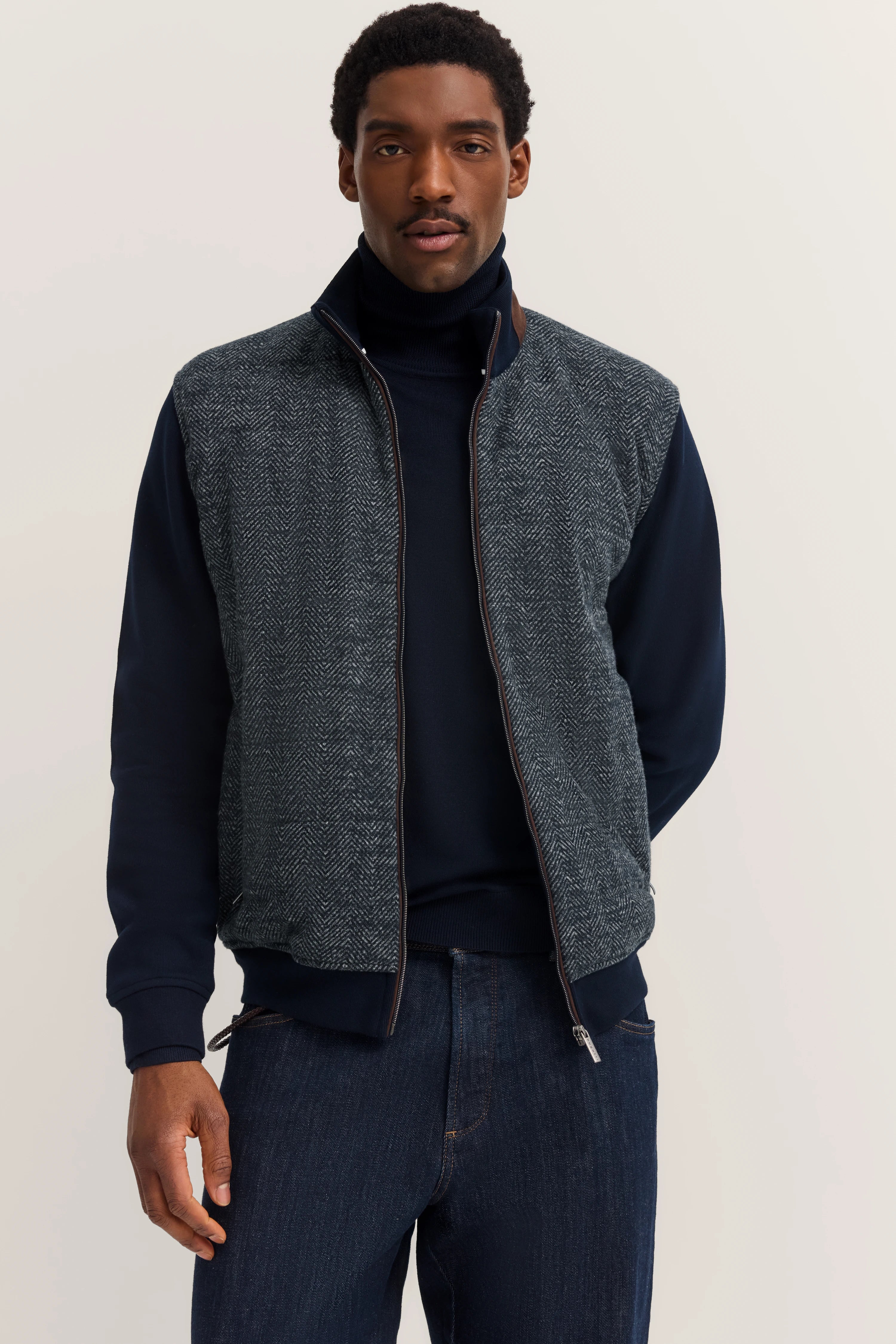 Modelbild: Mann in blauem Rollkragenpullover und grauer Weste mit Fischgrätenmuster von bugatti.