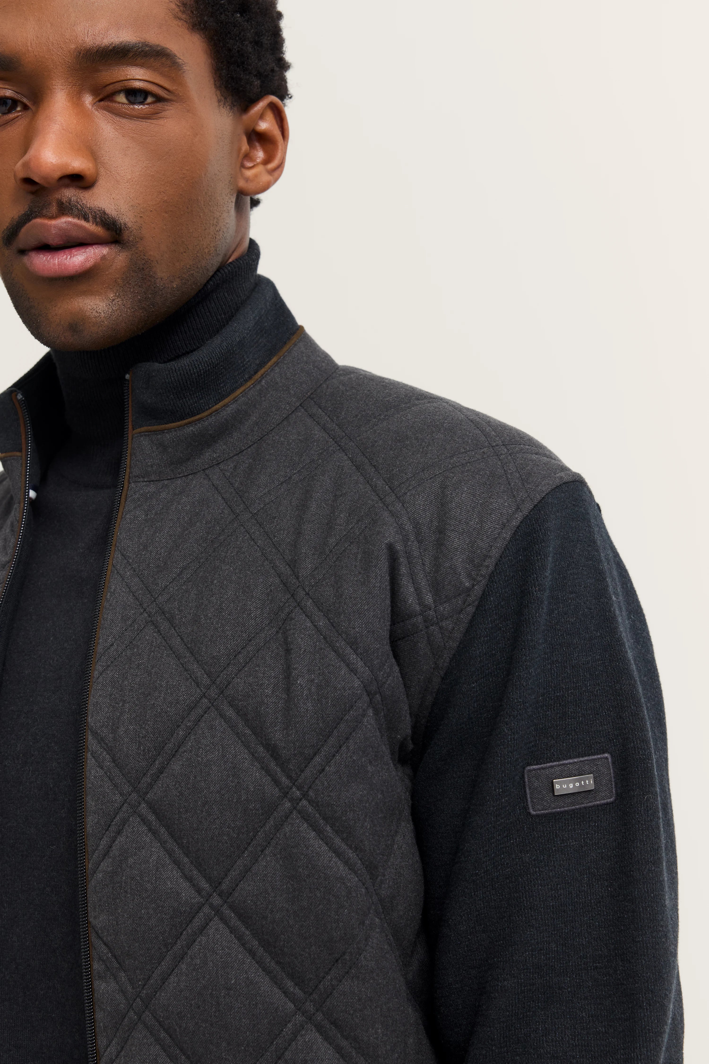 bugatti Herrenjacke, dunkelgrau, gesteppter Stoff, schwarzer Rollkragenpullover, Modelbild, entspannte Pose.