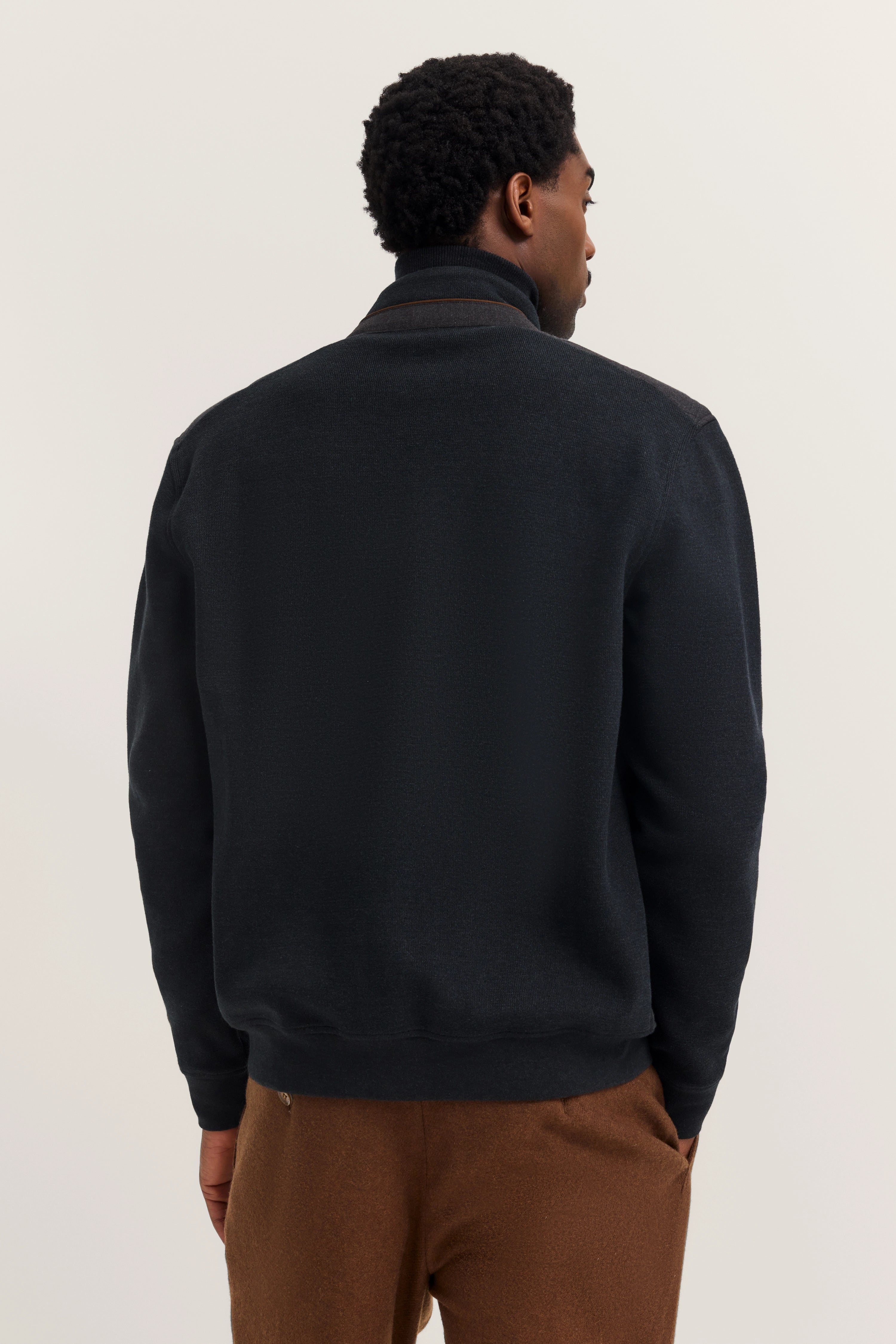 Schwarze bugatti Jacke, braune Hose, Model von hinten, lässige Haltung.