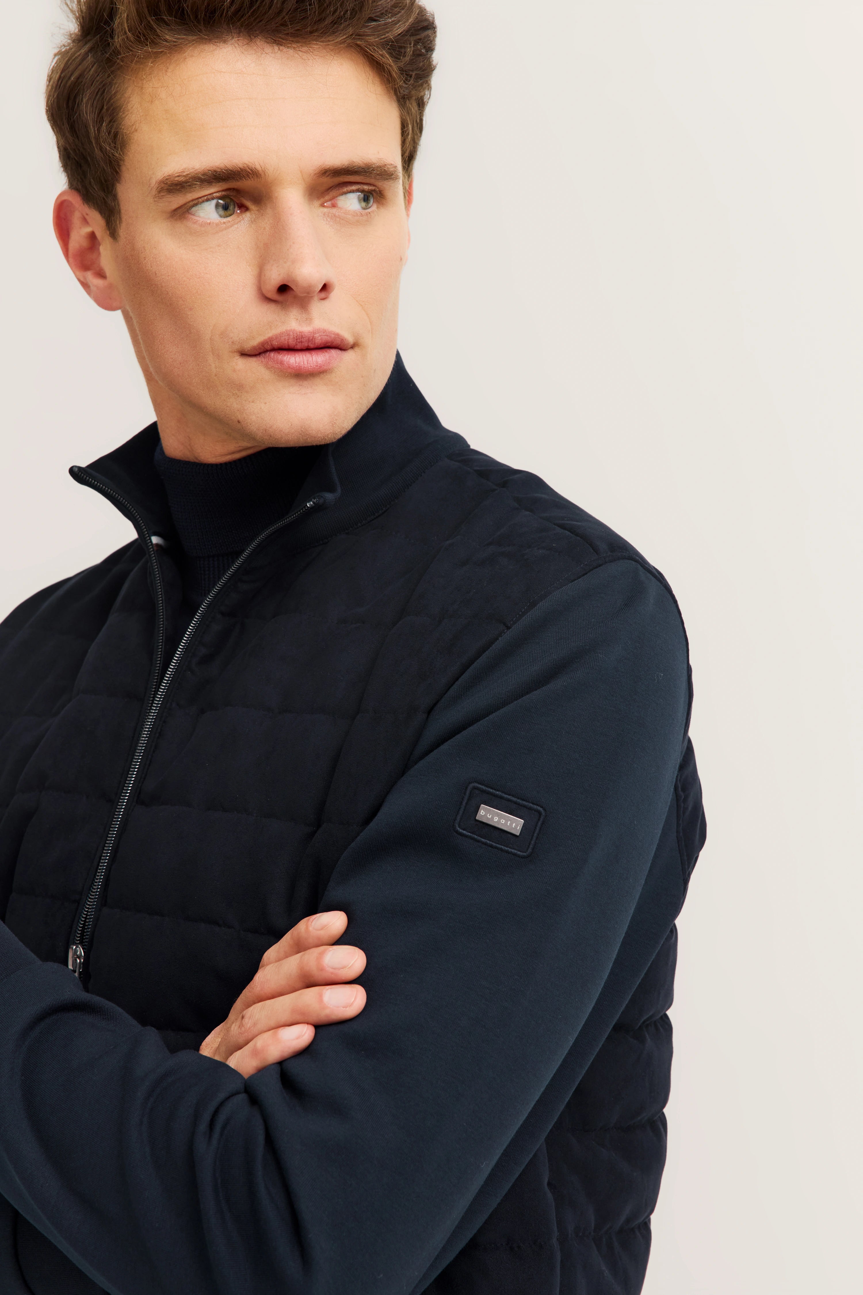 Modelbild: Mann in navy Steppjacke von bugatti, Arme verschränkt, seitlicher Blick.