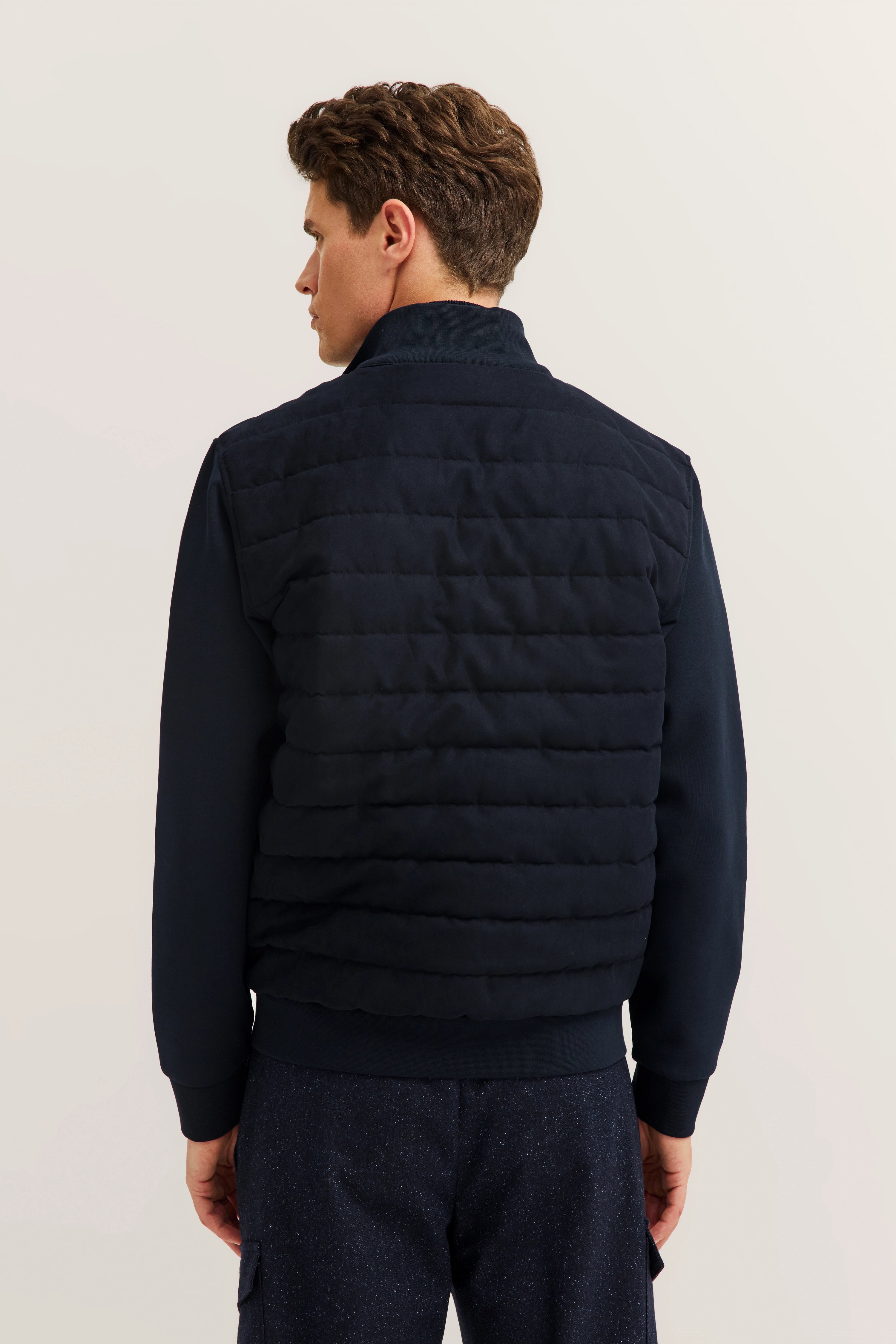 Model trägt eine dunkelblaue Steppweste und Hose von bugatti, Rückansicht, entspanntes Posing.