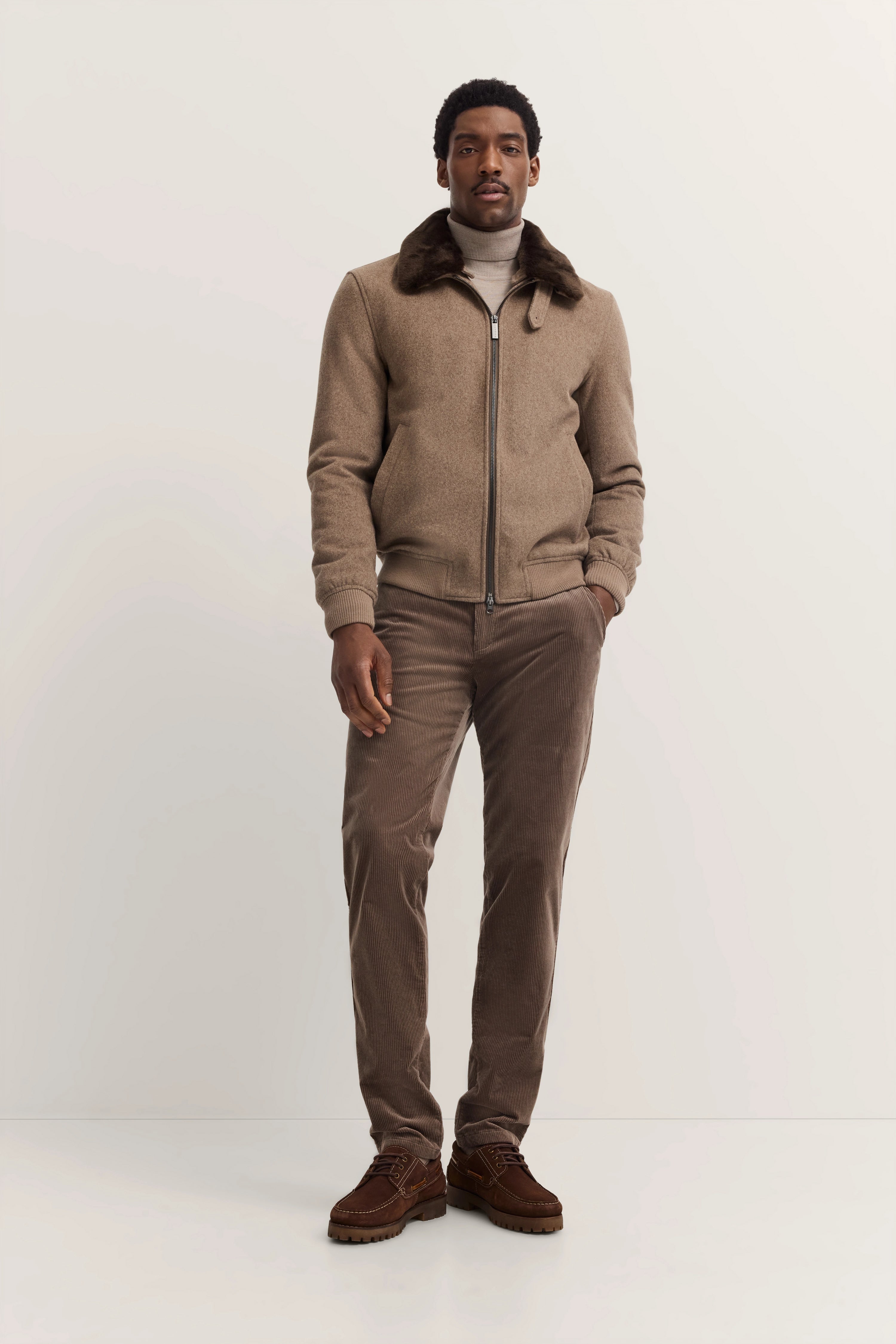 bugatti Modelbild: Braun melierte Jacke, grauer Rollkragen, braune Hose, braune Schuhe, entspannte Pose.