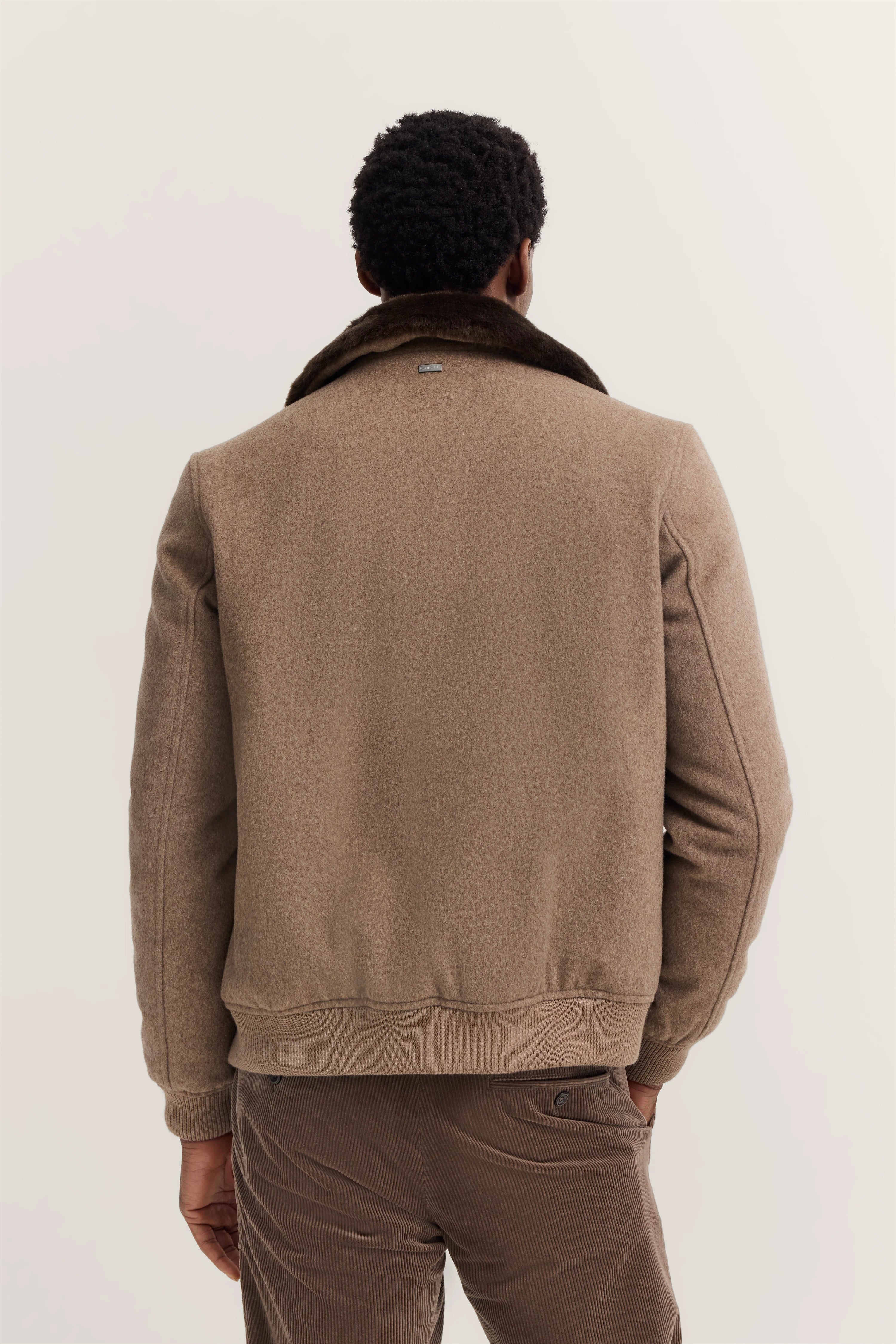 Rückansicht eines Models in brauner bugatti-Jacke mit Fellkragen und Cordhose.
