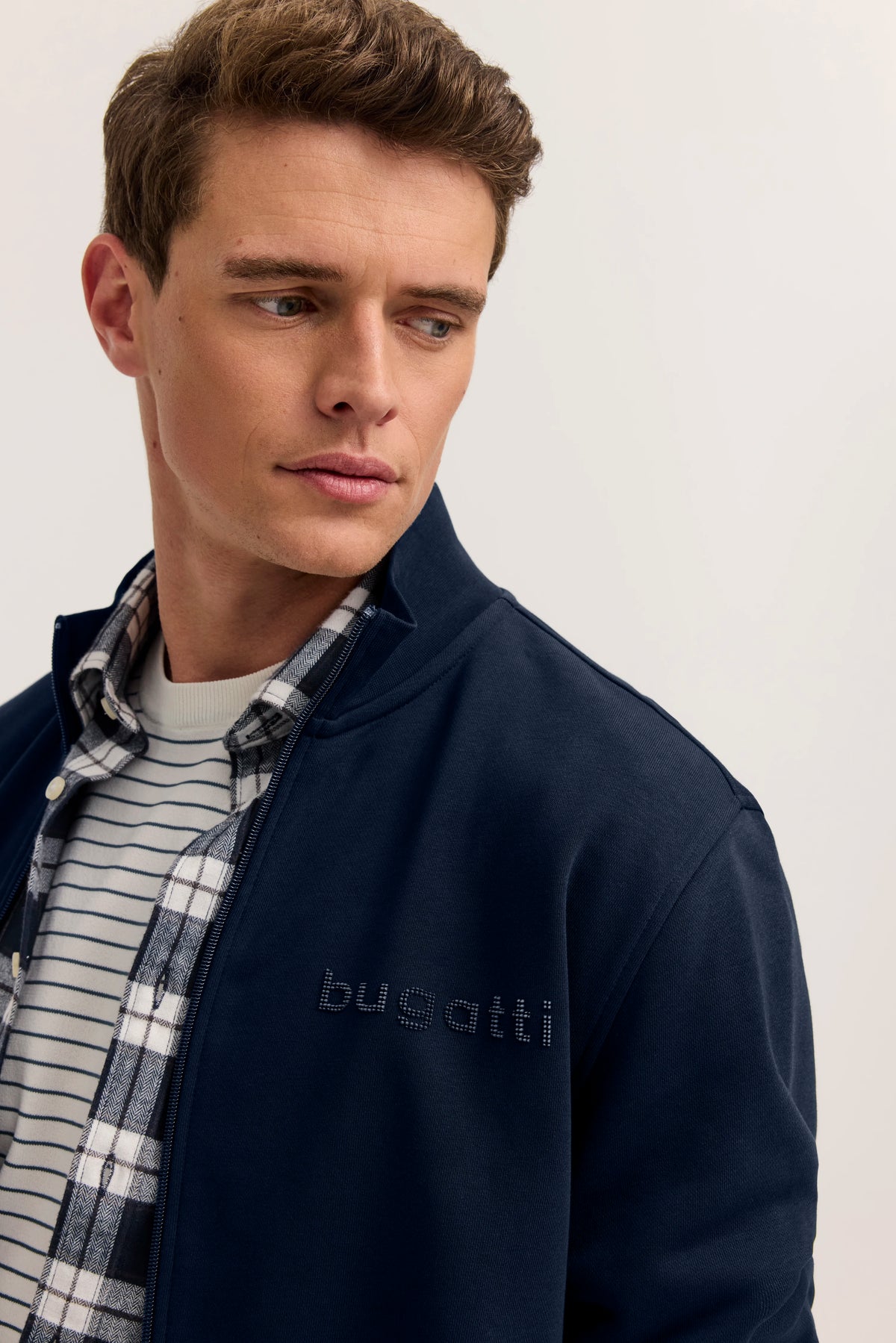 bugatti Jacke in Marineblau über gestreiftem Shirt, kariertes Hemd, Model seitlich blickend.