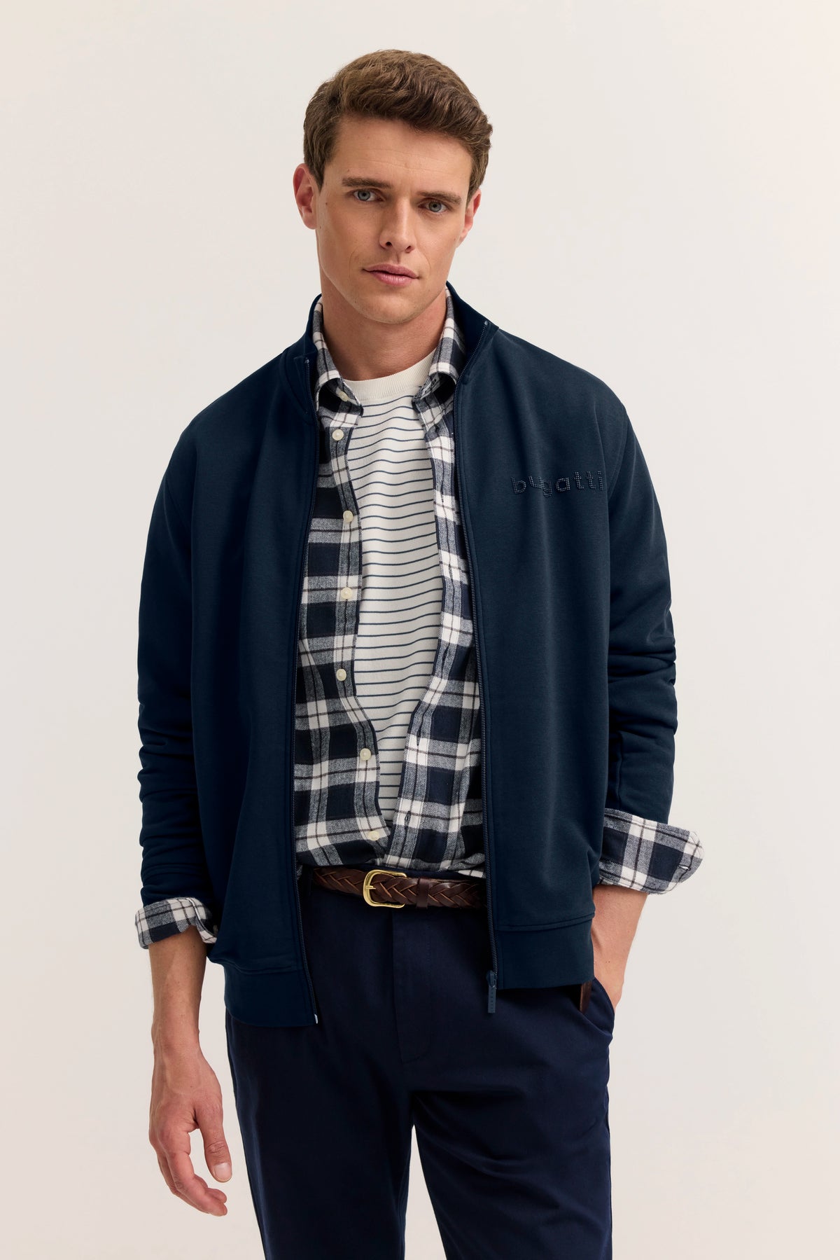 Model in bugatti-Outfit: Dunkelblauer Blouson, gestreiftes Shirt, karierte Hemd, marineblaue Hose.
