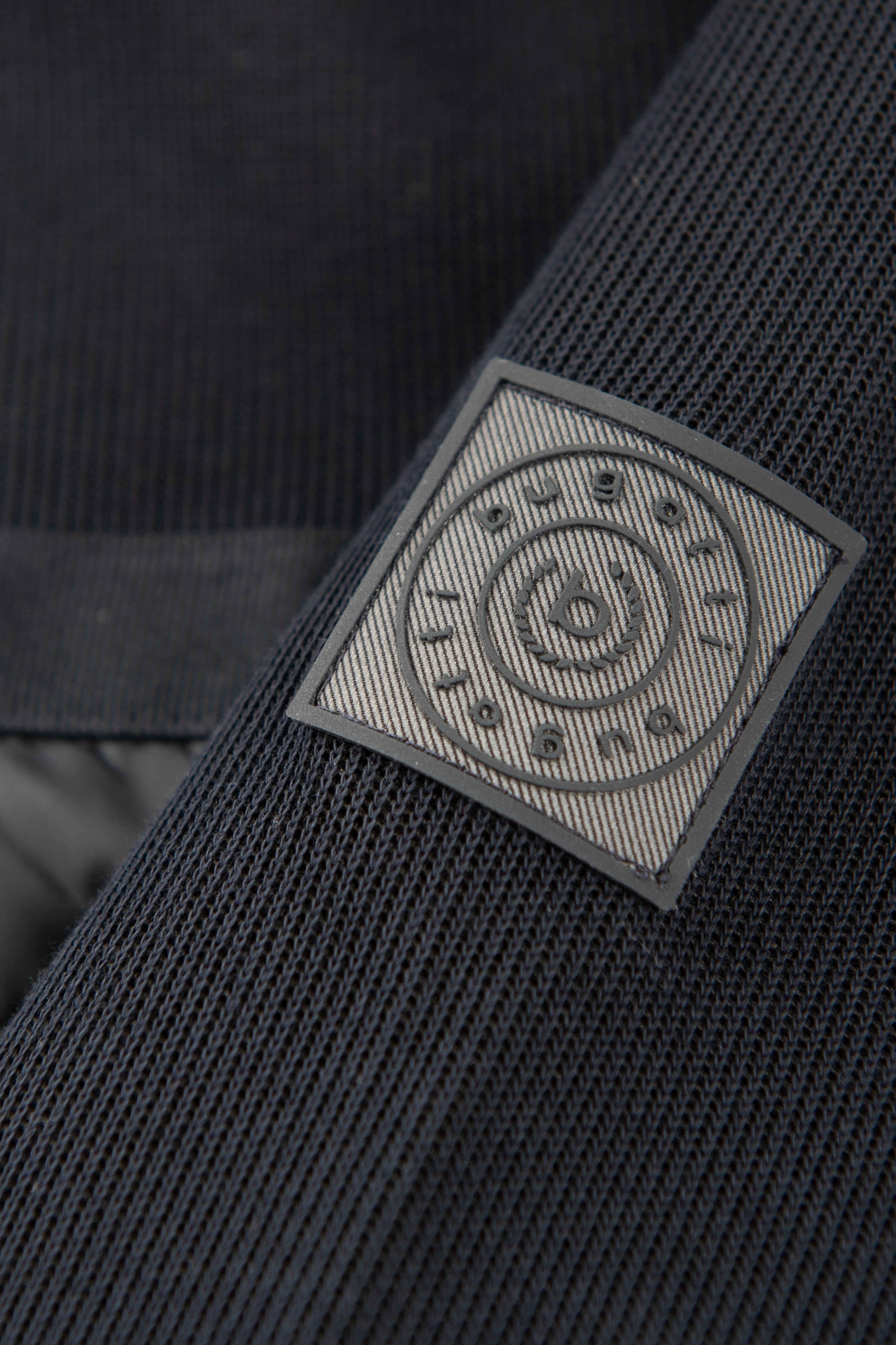 Schwarzer bugatti Strickstoff mit eingeprägtem Logo-Patch, Detailaufnahme.