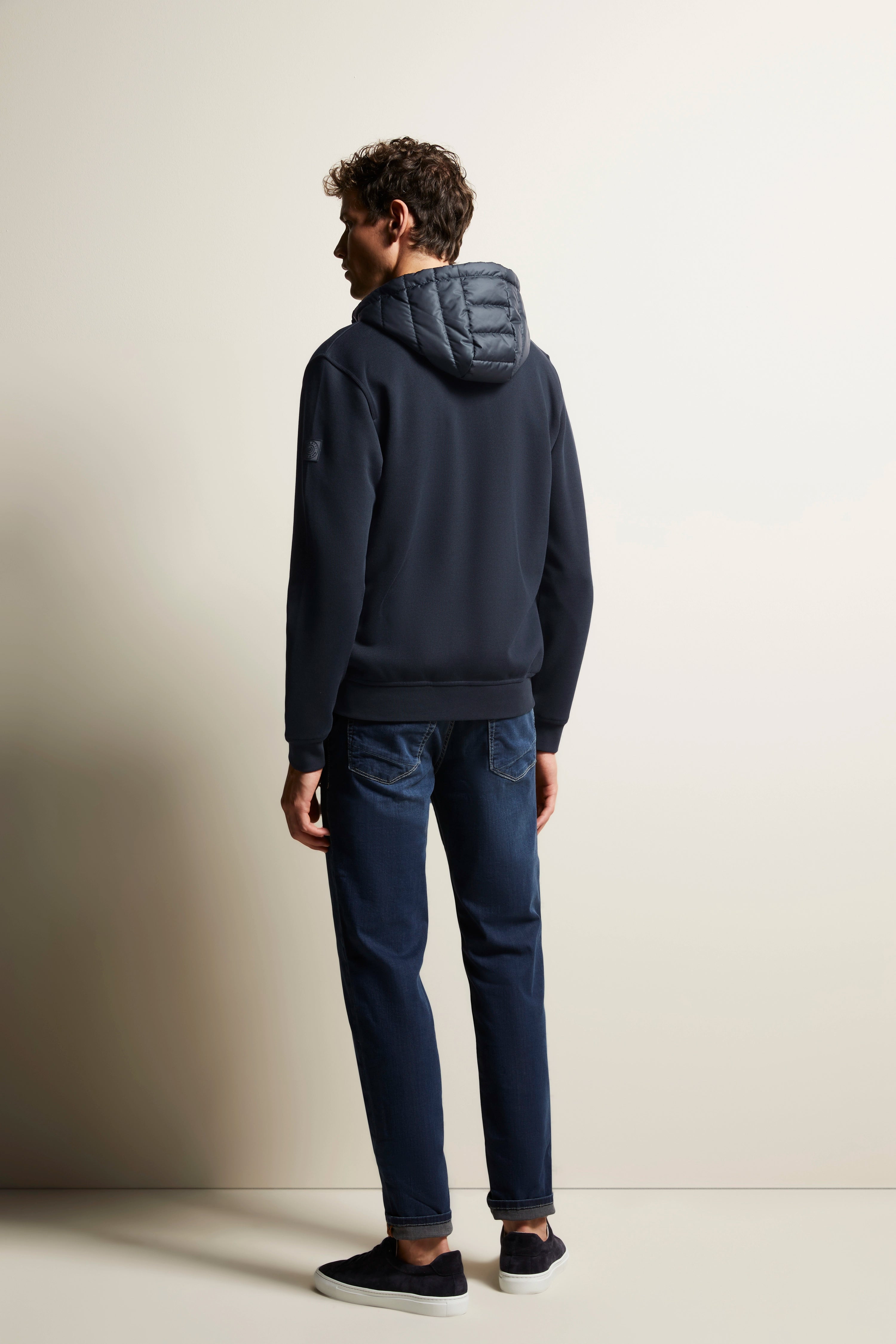 Model in dunkelblauer bugatti Hoodie und Jeans, von hinten, legeres Posing.