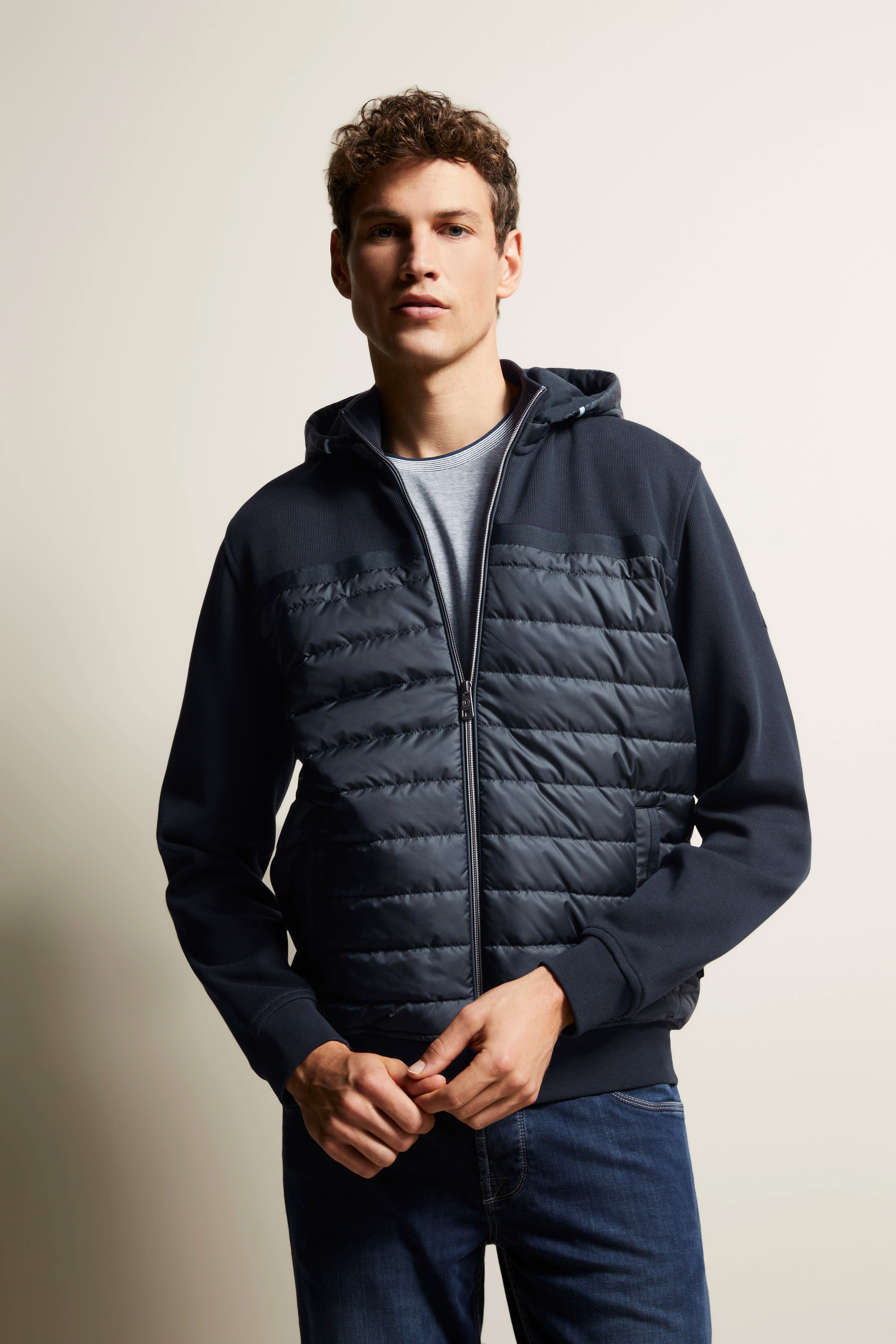 bugatti Modelbild mit dunkelblauer Steppjacke, lässig geschlossenes Posing, entspannter urbaner Stil.