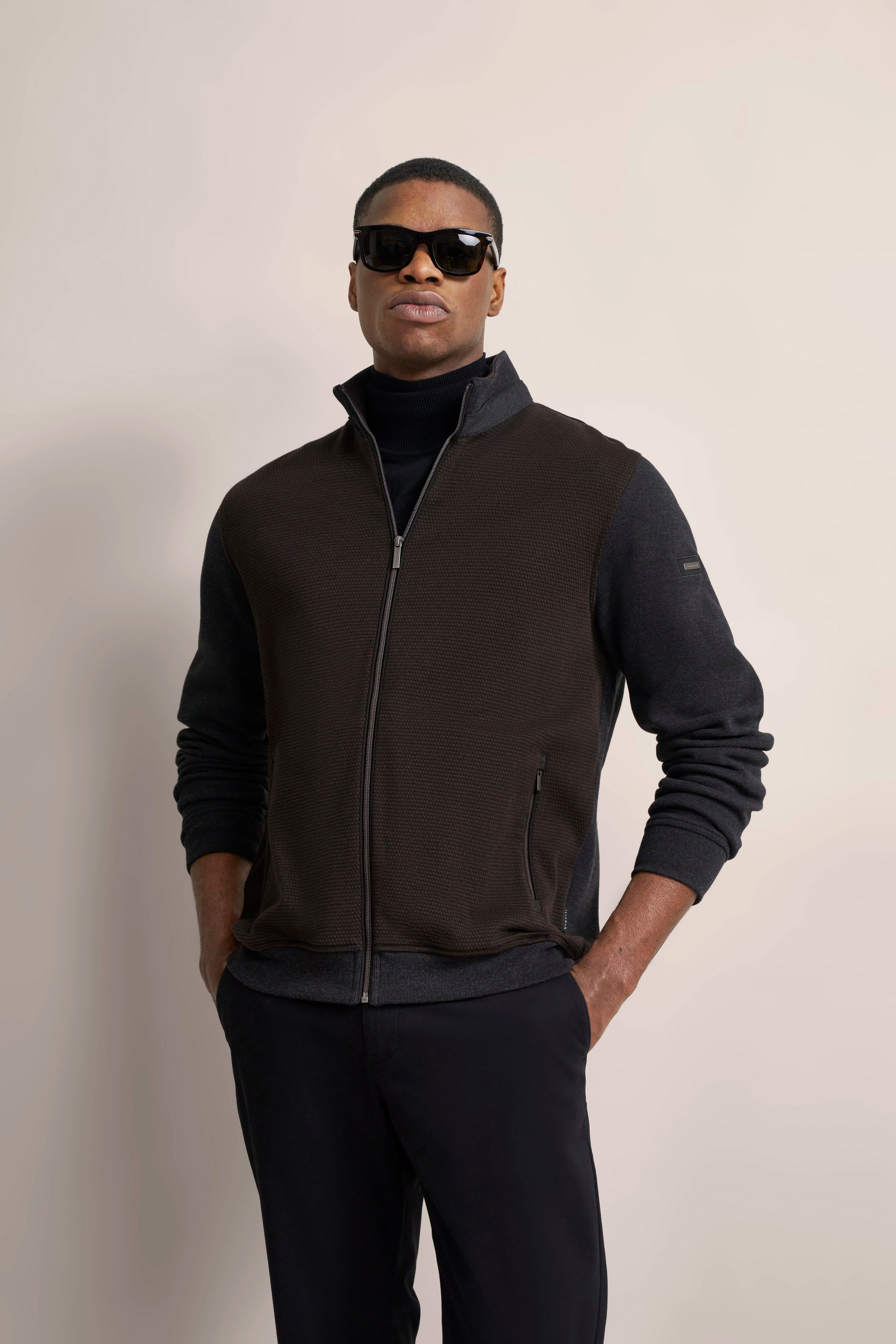 Model trägt braune Weste und schwarzen Rollkragen von bugatti, lässige Pose mit Händen in den Hosentaschen.