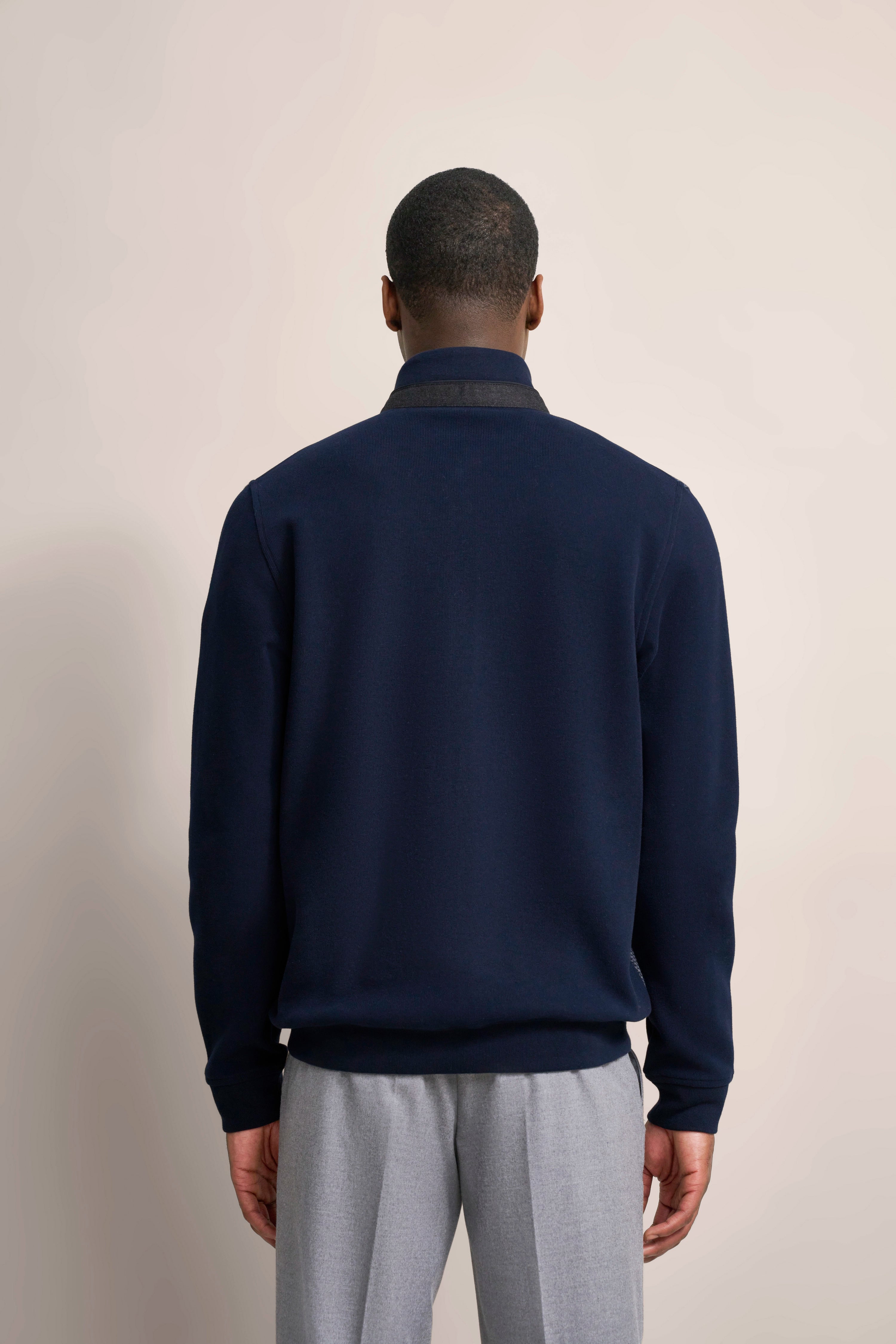 bugatti Modelbild: Dunkelblauer Pullover und graue Hose, Rückenansicht, lässiges Stehen.