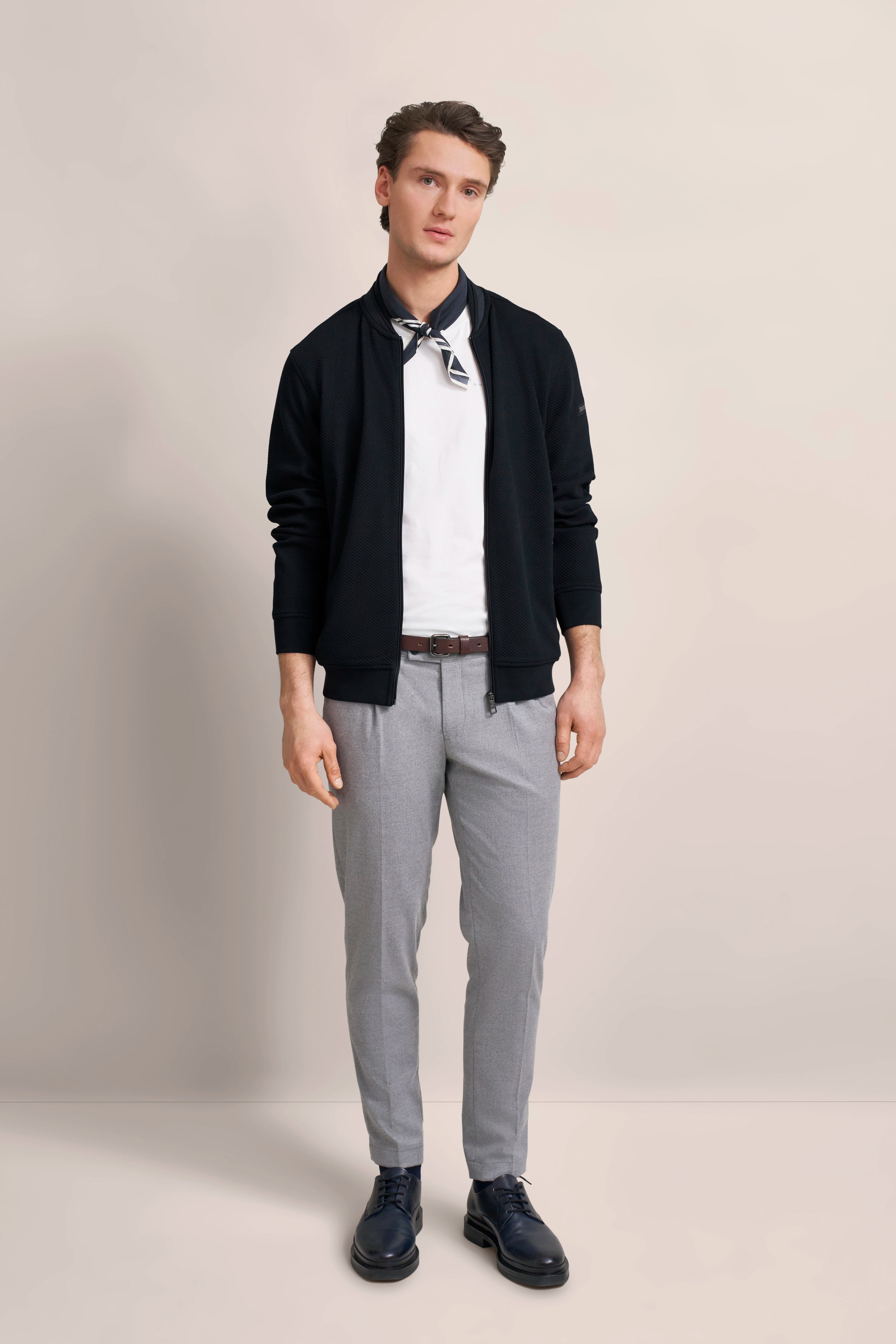Model in schwarzer Jacke, weißem Shirt und grauer Hose von bugatti, legeres Posing, eleganter Stil.