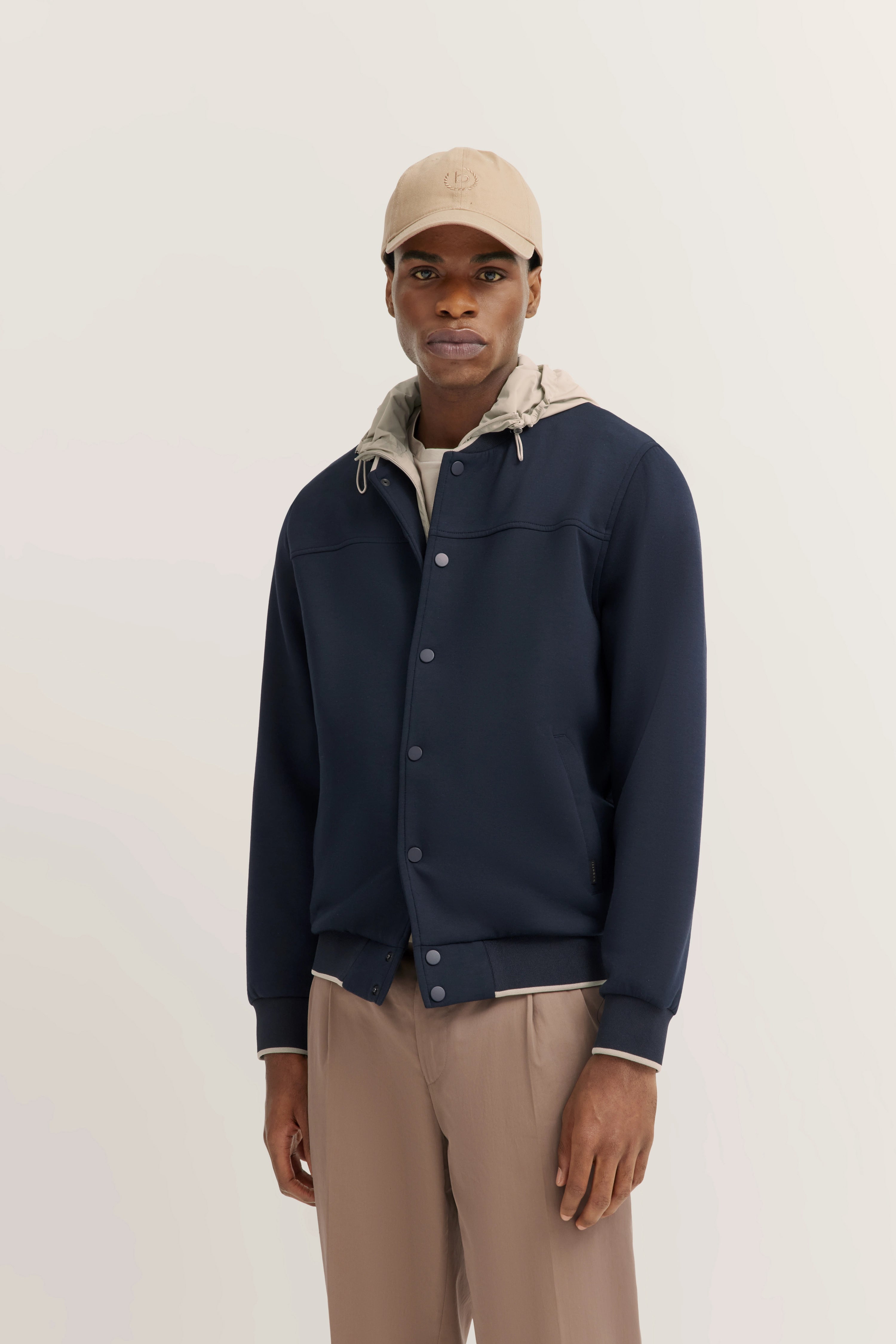 Model in navy bugatti Jacke, beige Kapuze und Hose, lässiger Stand.