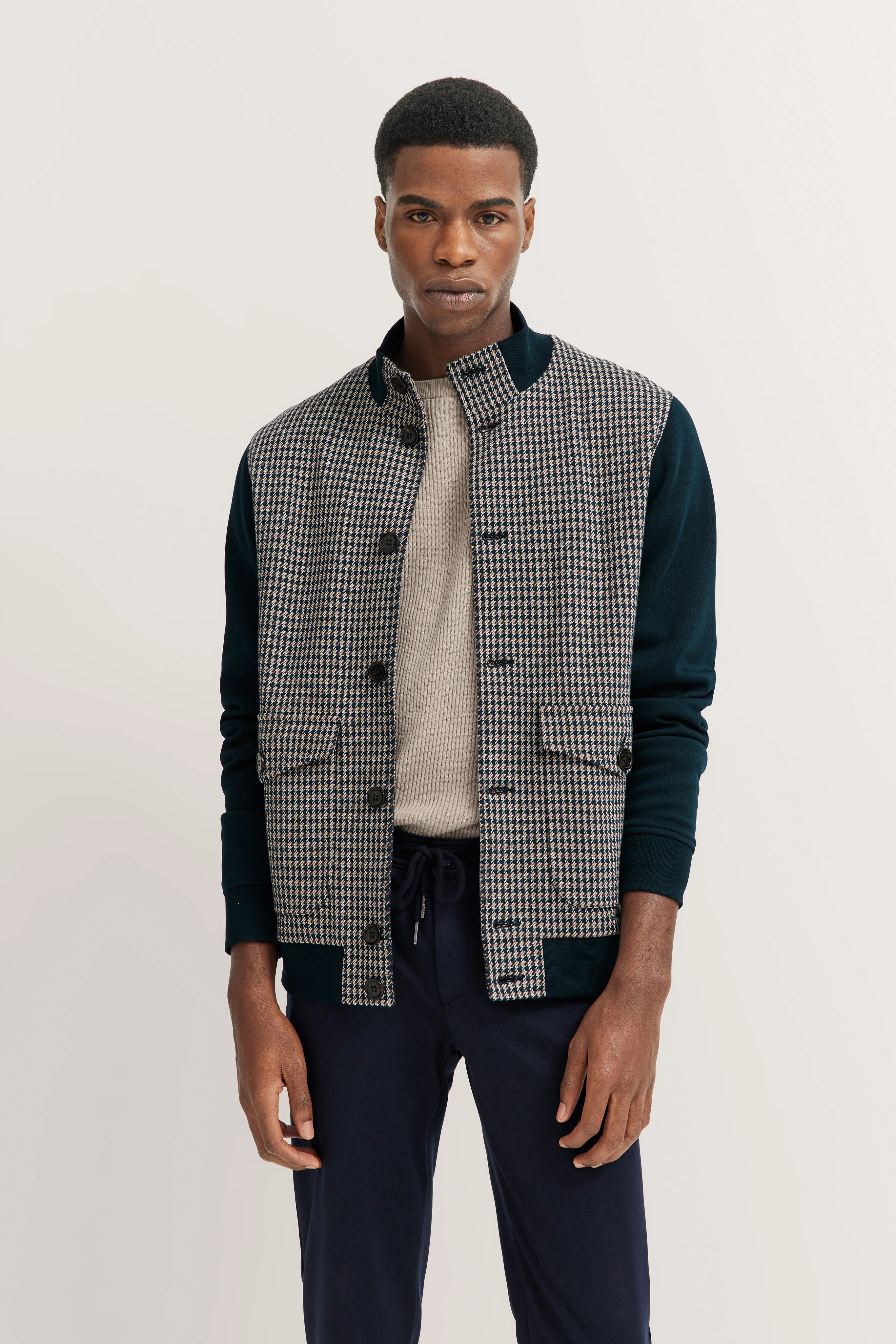 Model in bugatti Blouson mit Hahnentrittmuster, cremefarbenem Pullover, dunklen Hosen, lässige Pose.