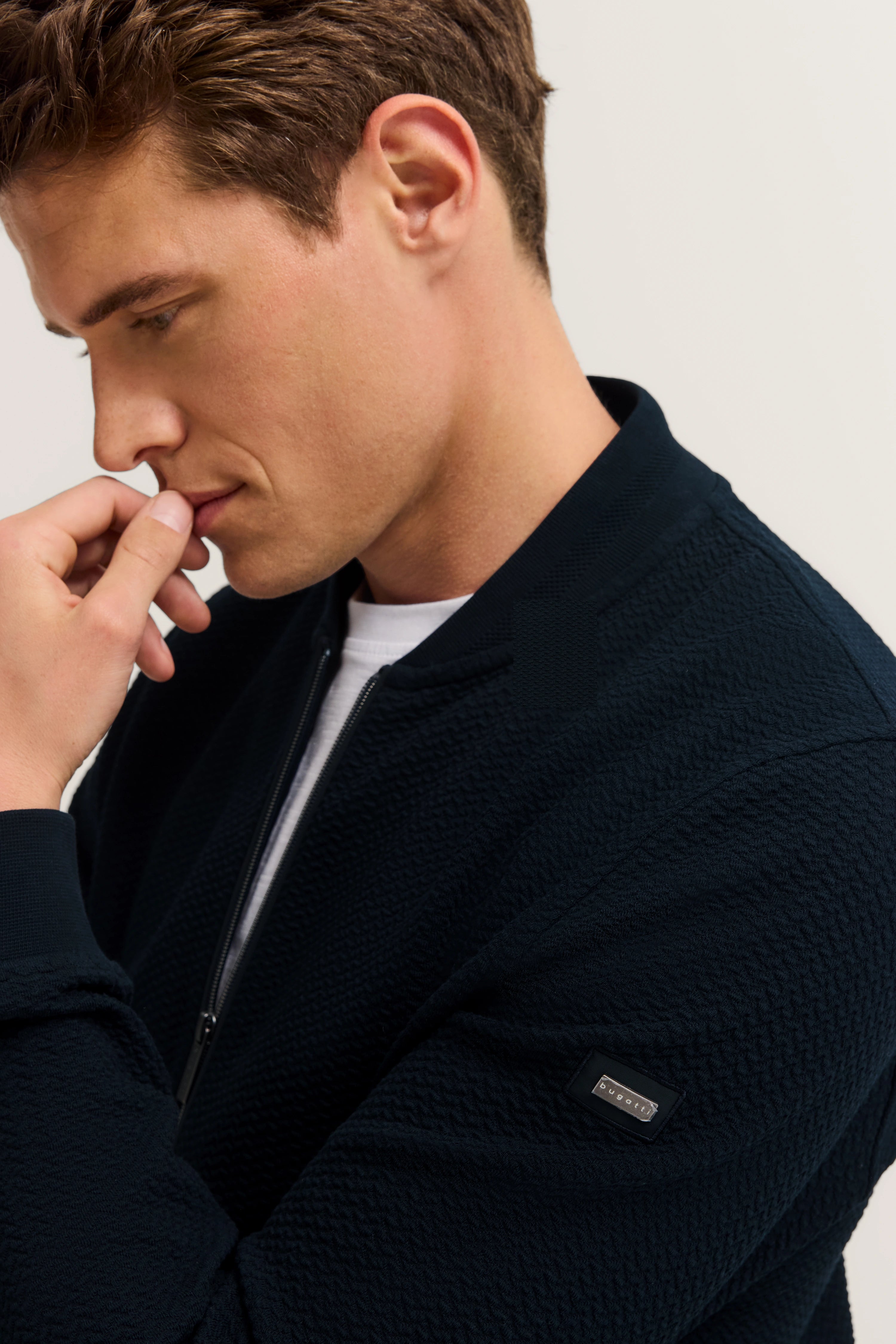 Model in dunkelblauer bugatti-Jacke, nachdenkliche Pose, seitliches Büstenbild.