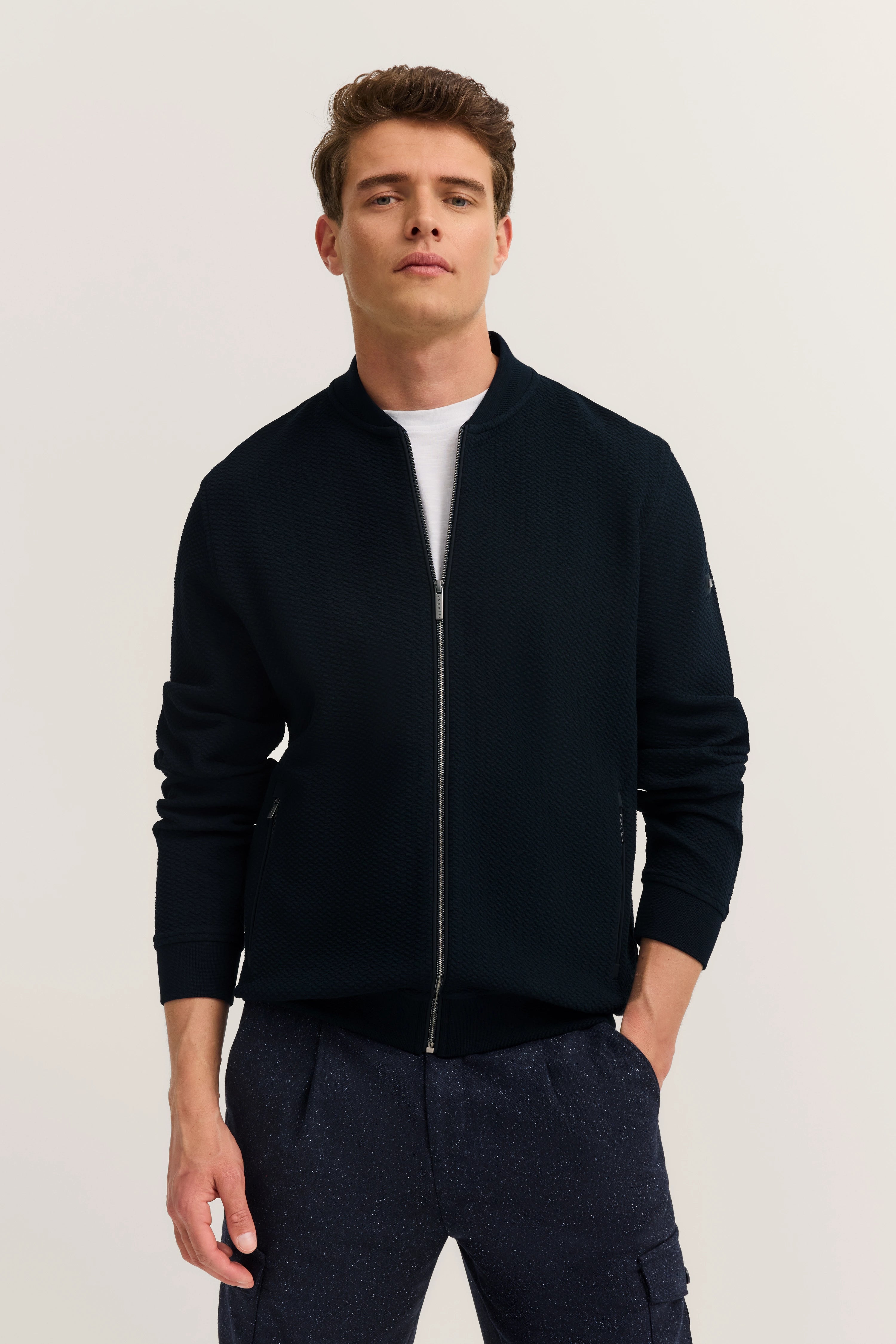 Männermodell in dunkelblauer bugatti Jacke, legeres Posing, weiße T-Shirt Details sichtbar.
